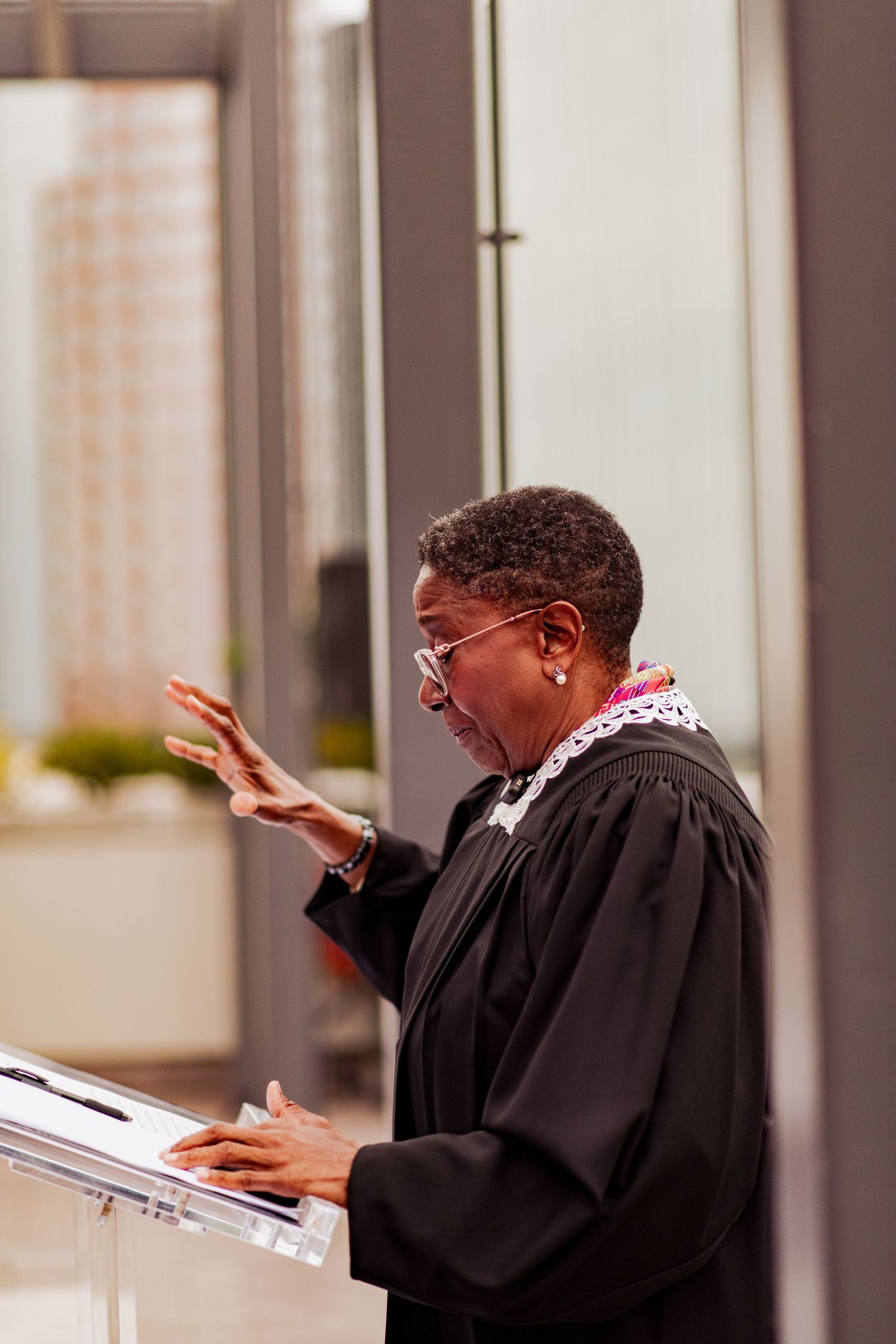 A person in black robes gestures expressively while speaking at a formal ceremony.