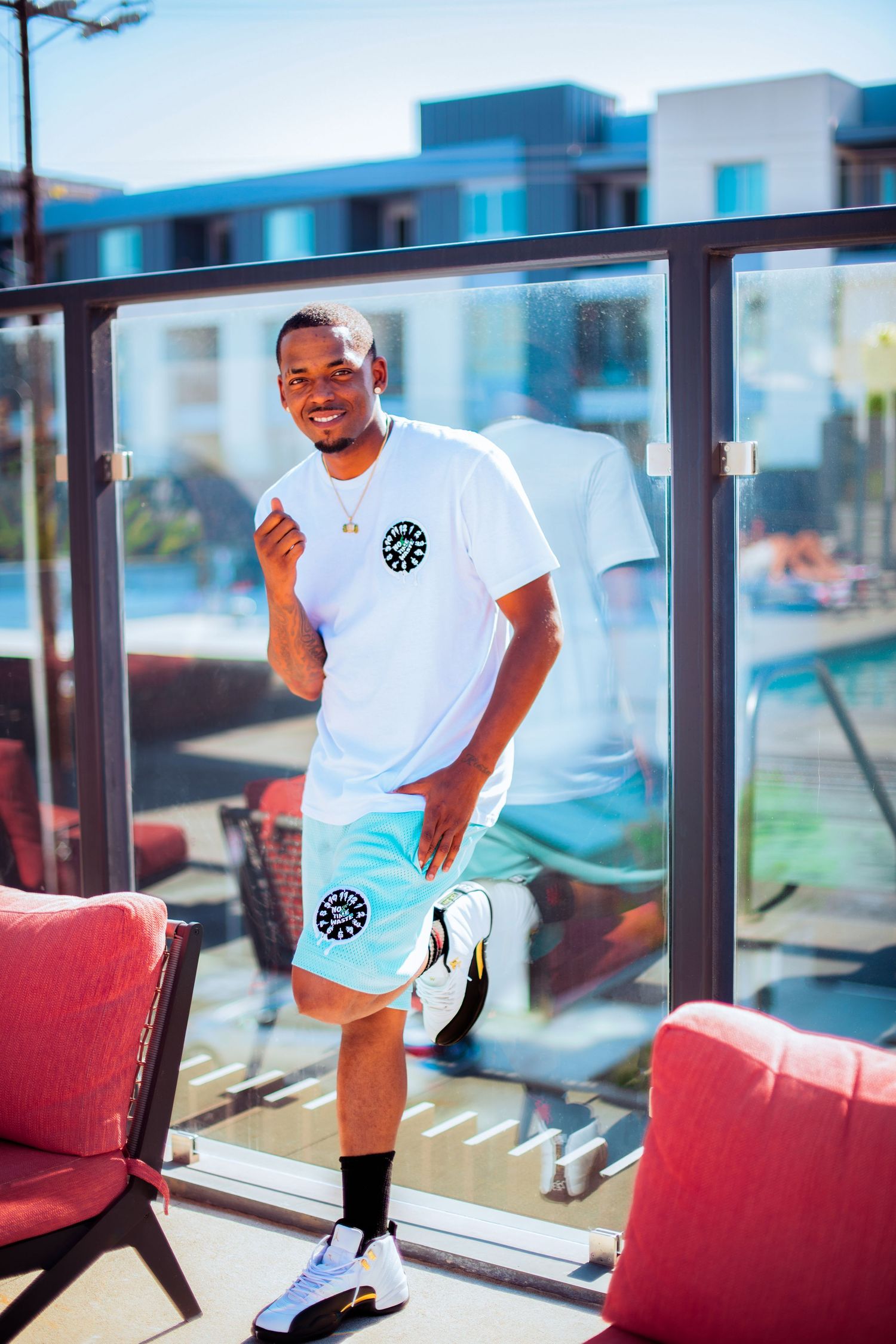 A person in white t-shirt and shorts poses in front of large windows with red chairs.