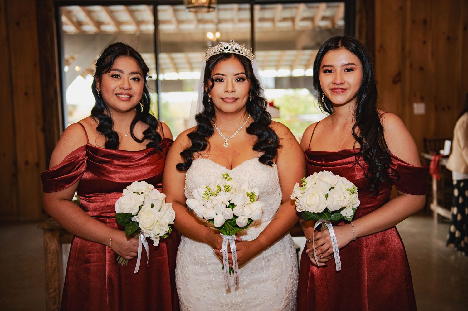 Wedding party in burgundy dresses and formal attire posing together indoors with white floral bouquets.