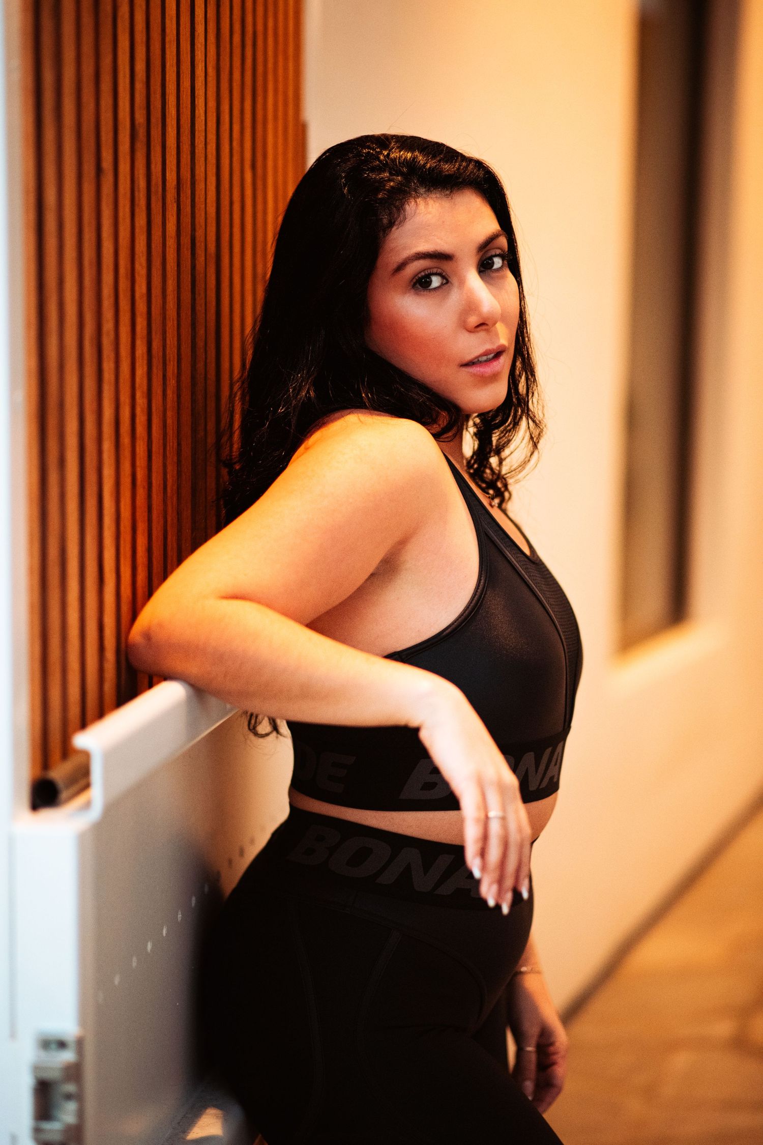 Woman in black athletic wear poses gracefully in warm interior lighting.
