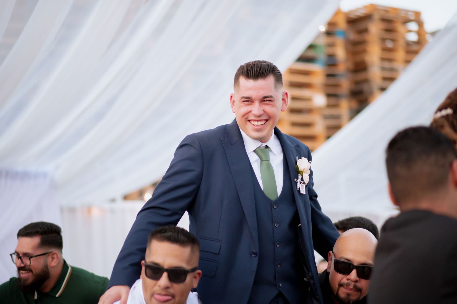 Groomsmen and guests in suits and sunglasses gathered during wedding celebration.