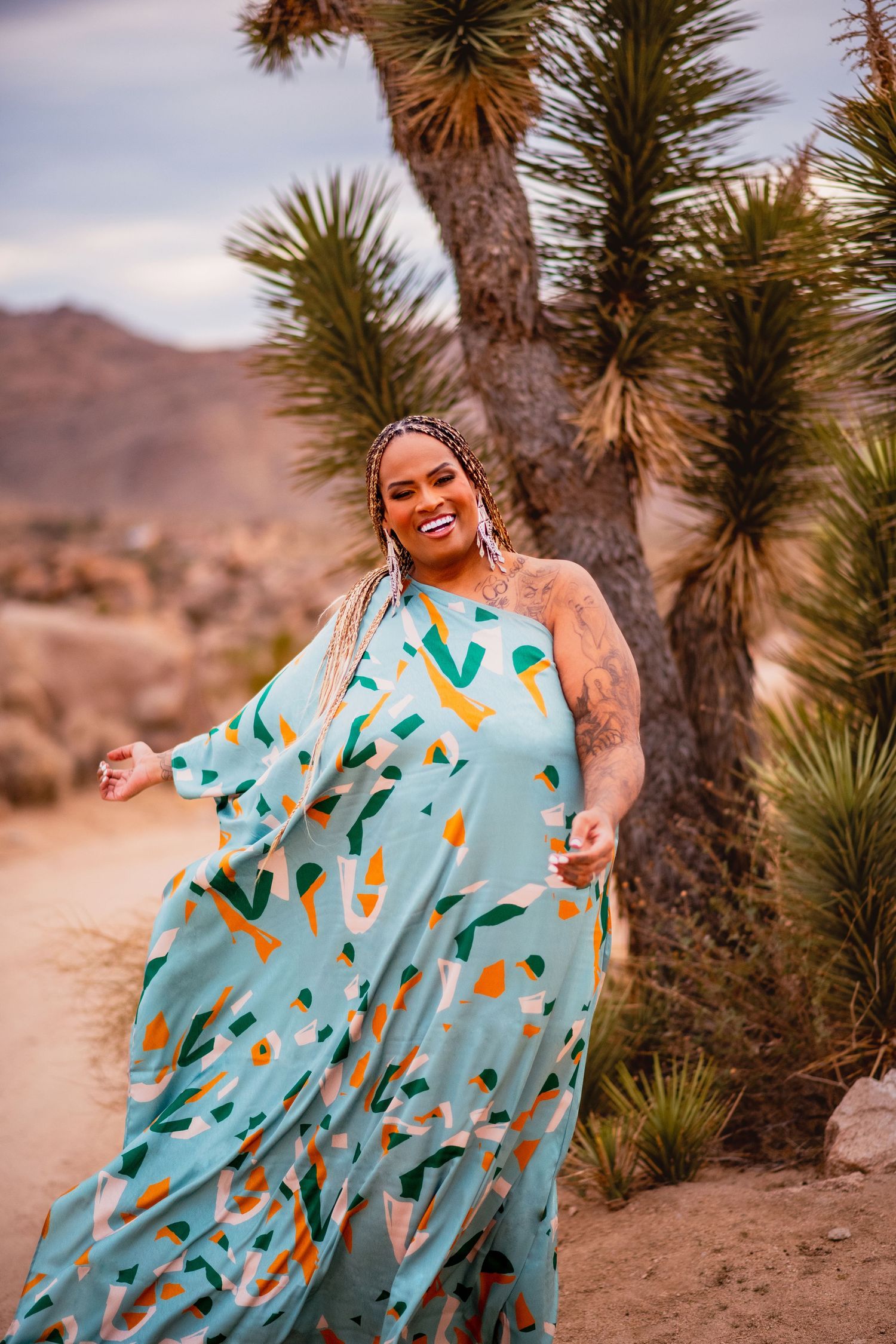 A turquoise patterned dress twirls dramatically against a desert landscape with yucca plants.