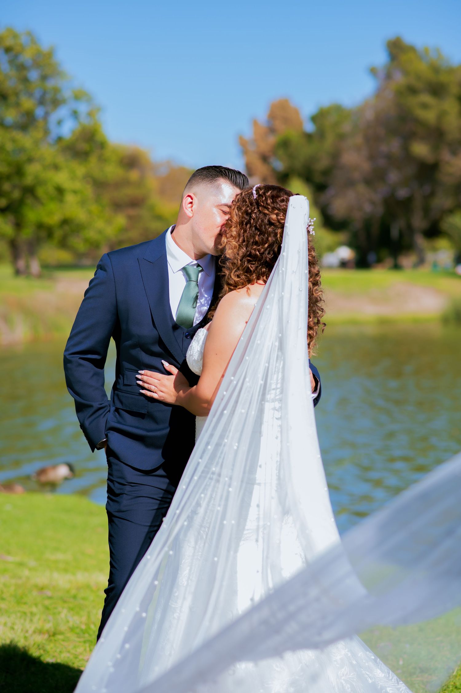 Elegant wedding photos by lake showing flowing veil movement and natural scenery.