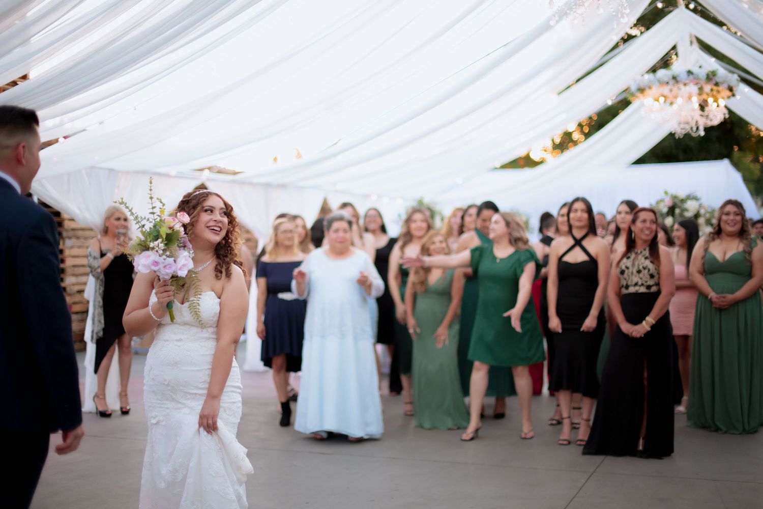 Large group of wedding guests dancing and celebrating under a decorated white tent.