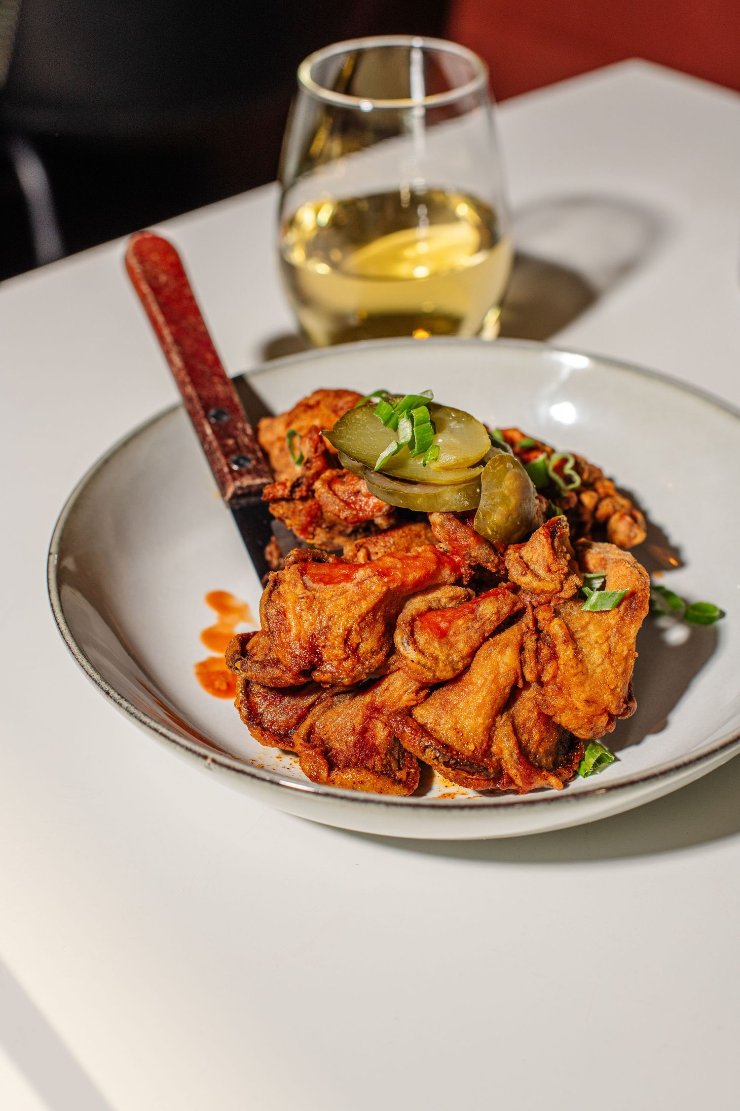 Spicy buffalo chicken wings garnished with celery and pickles on a white plate with golden wine.