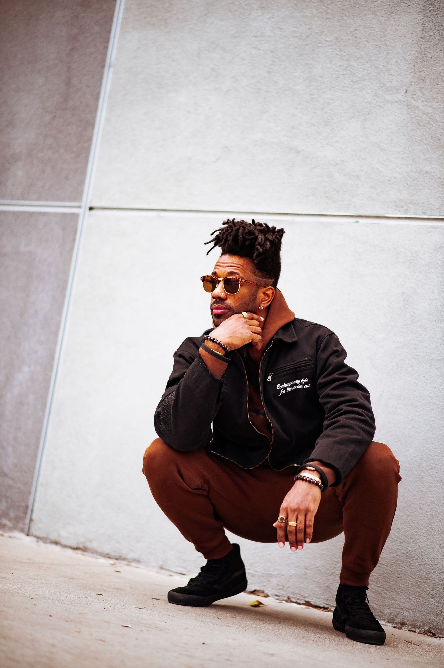 Person in sunglasses and dark clothing crouches against a light-colored wall in an artistic photo series.