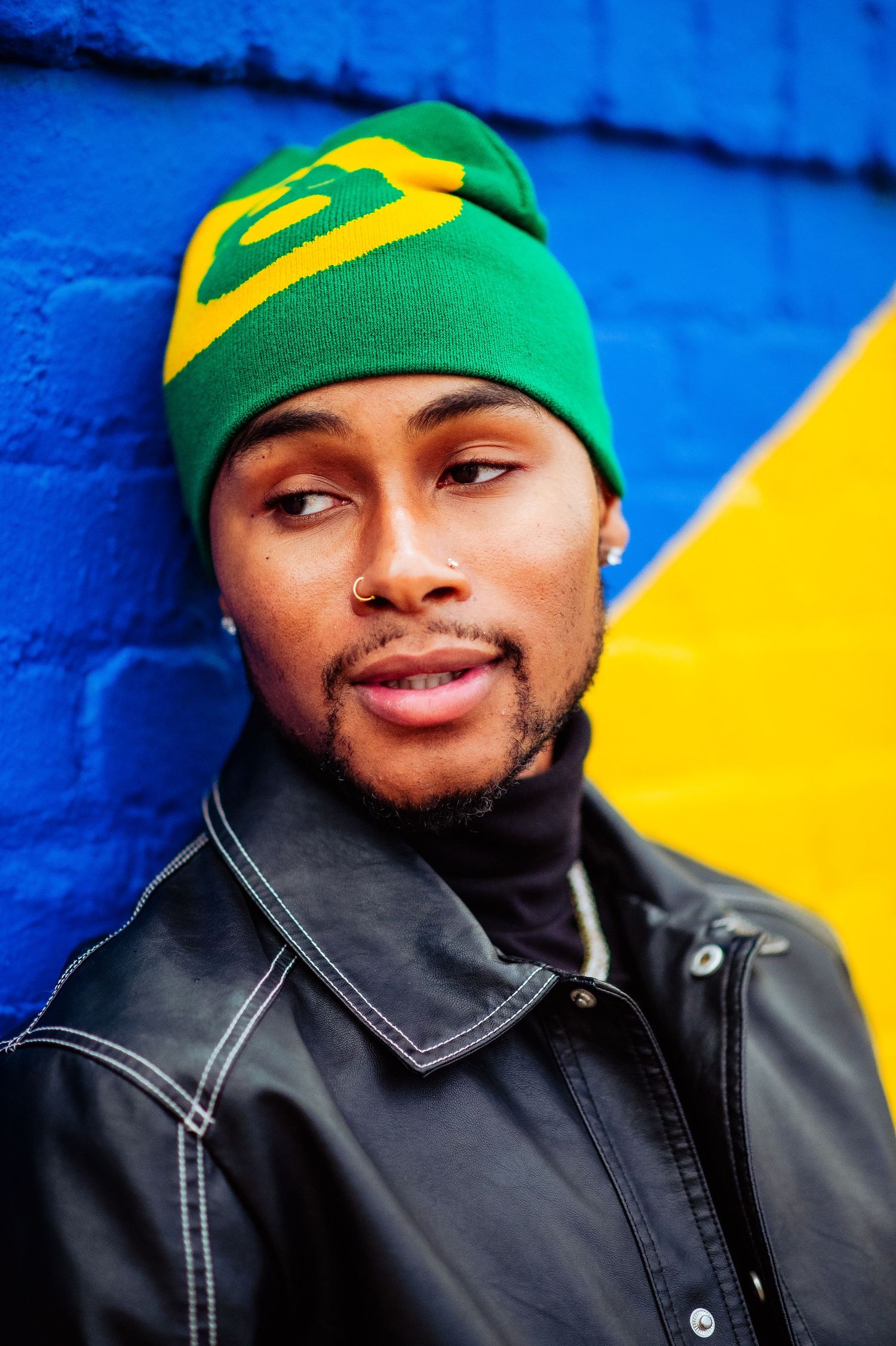 Paris B newfaceofrnb_
wearing green and yellow beanie with black jacket against vibrant blue and yellow wall. LA Arts District.