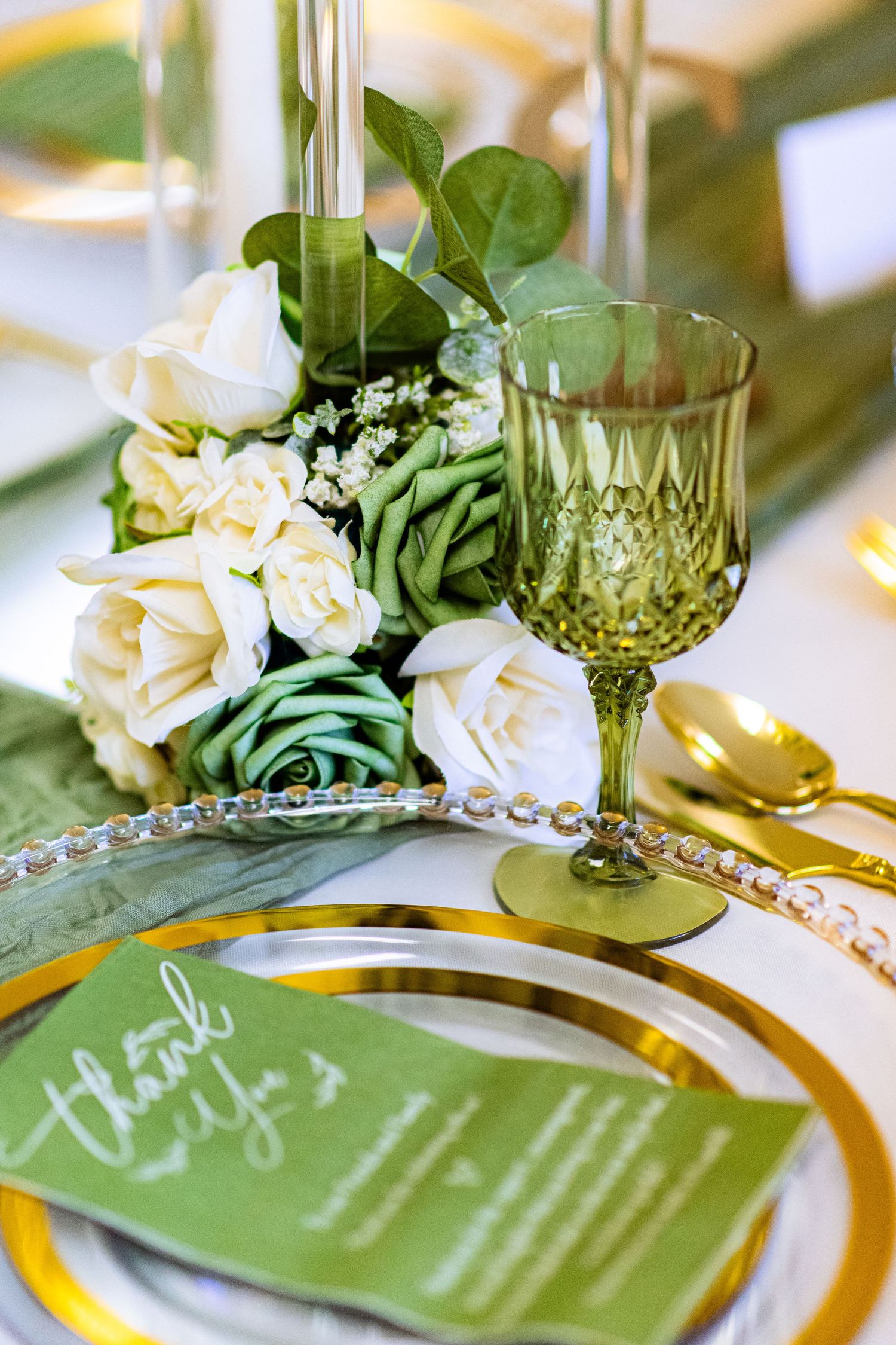 Elegant wedding table settings with green menus, gold chargers, and white floral arrangements.