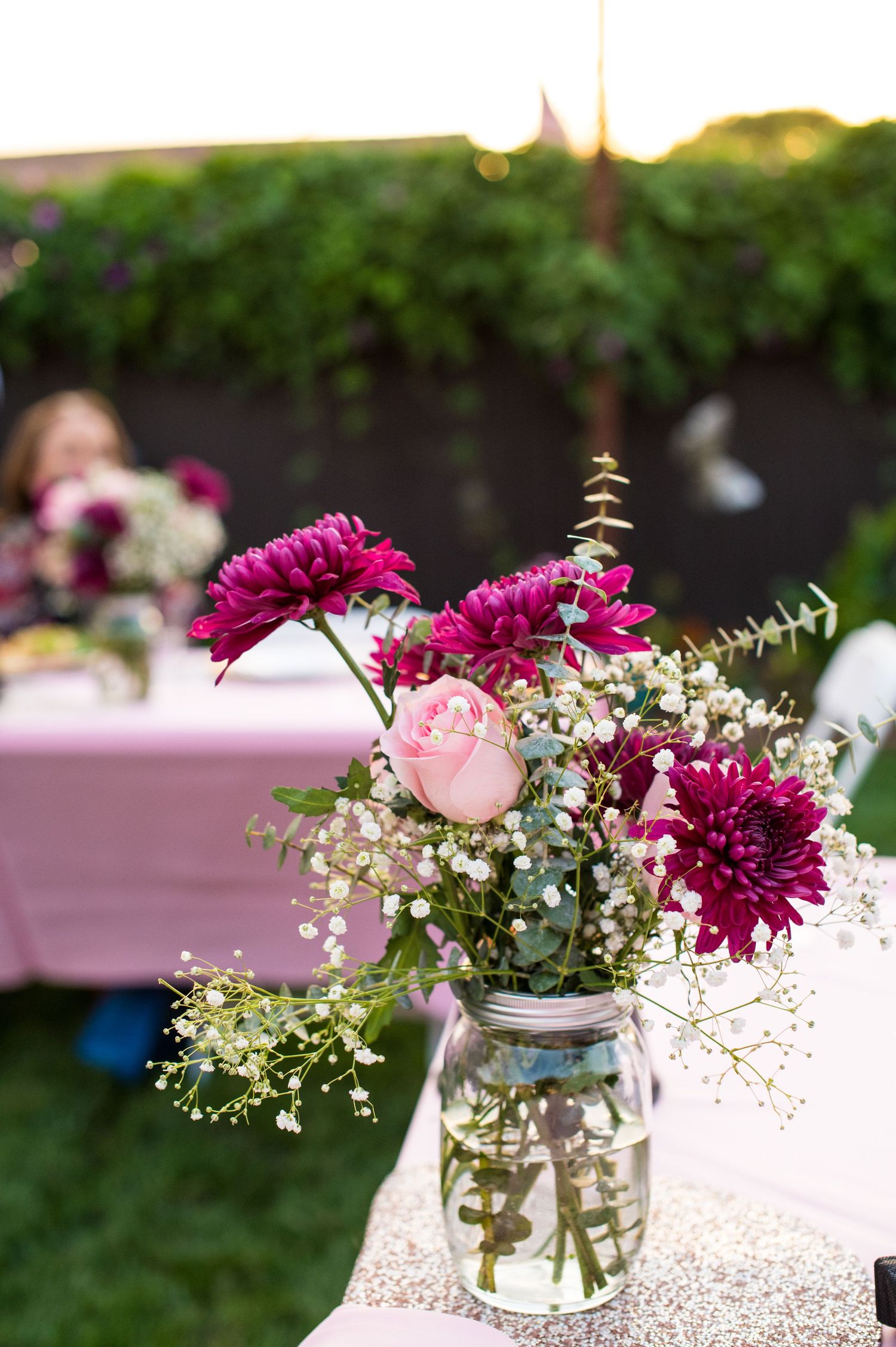 Mason jars filled with pink and purple flowers create romantic centerpieces with delicate baby's breath accents.