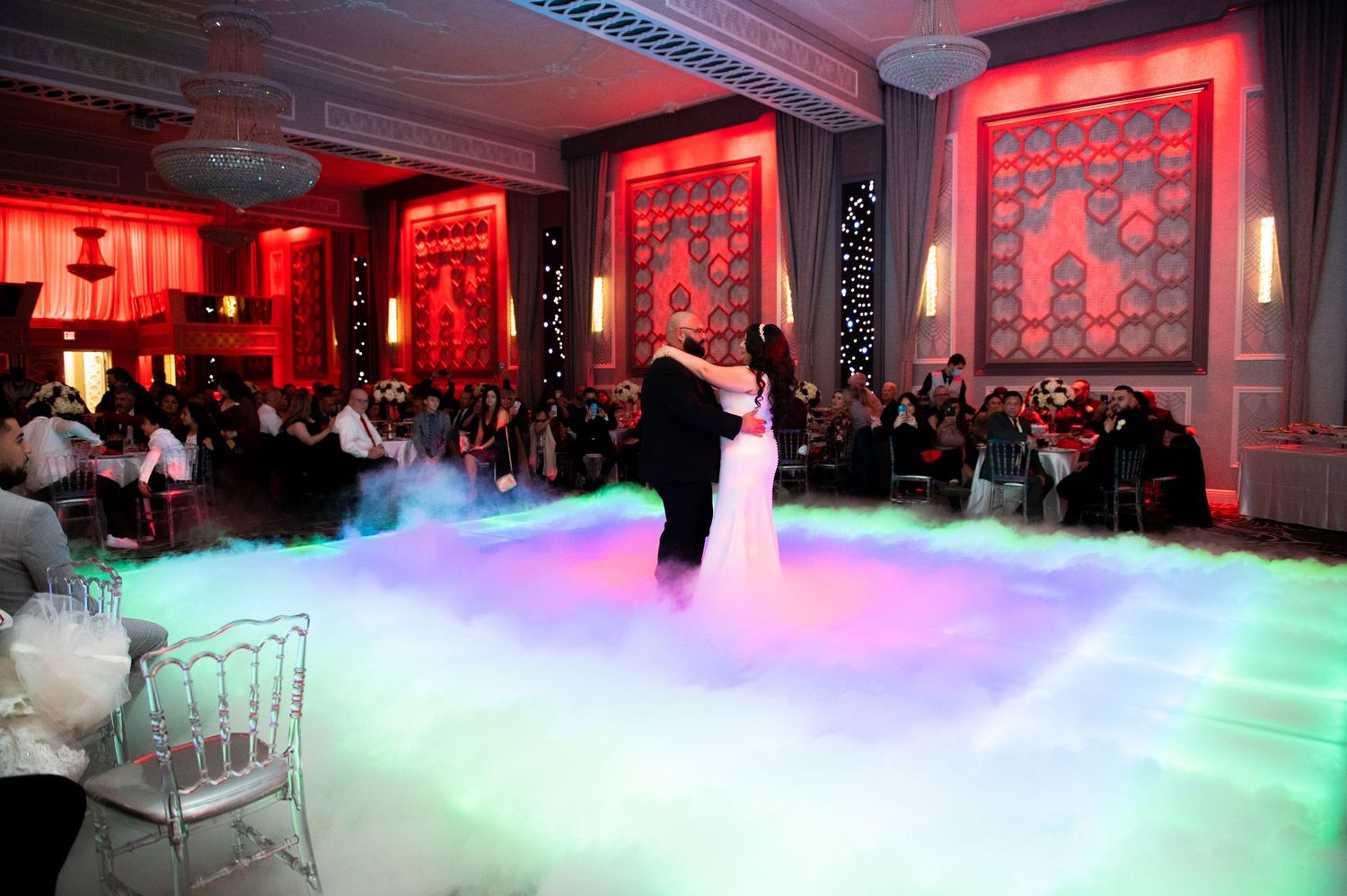 A wedding reception venue features dramatic lighting effects with red uplighting and fog on the dance floor.