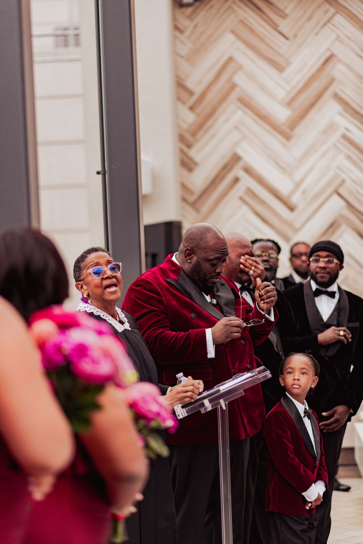 Wedding guests in formal attire react emotionally during a ceremony in an elegant venue.