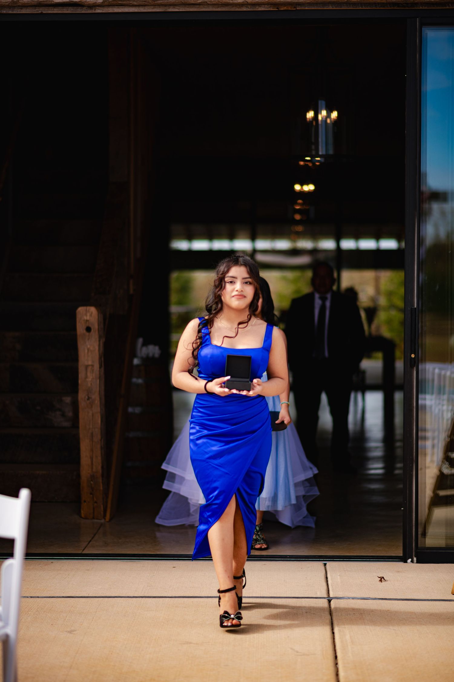 A person in a royal blue formal dress walks through a doorway holding a wine glass at an elegant event.