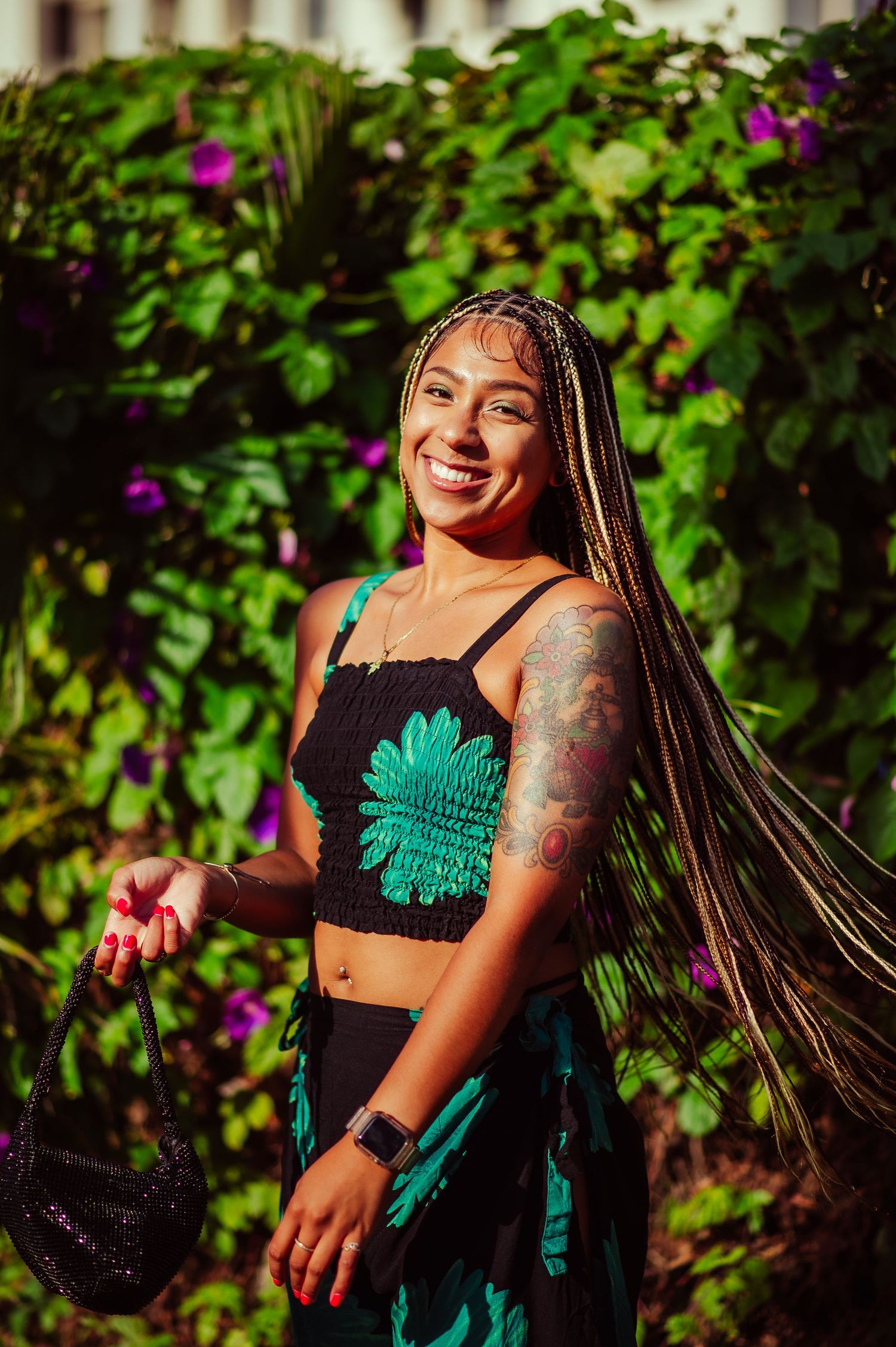 Outdoor fashion photography with lush greenery and bright purple flowers in background.