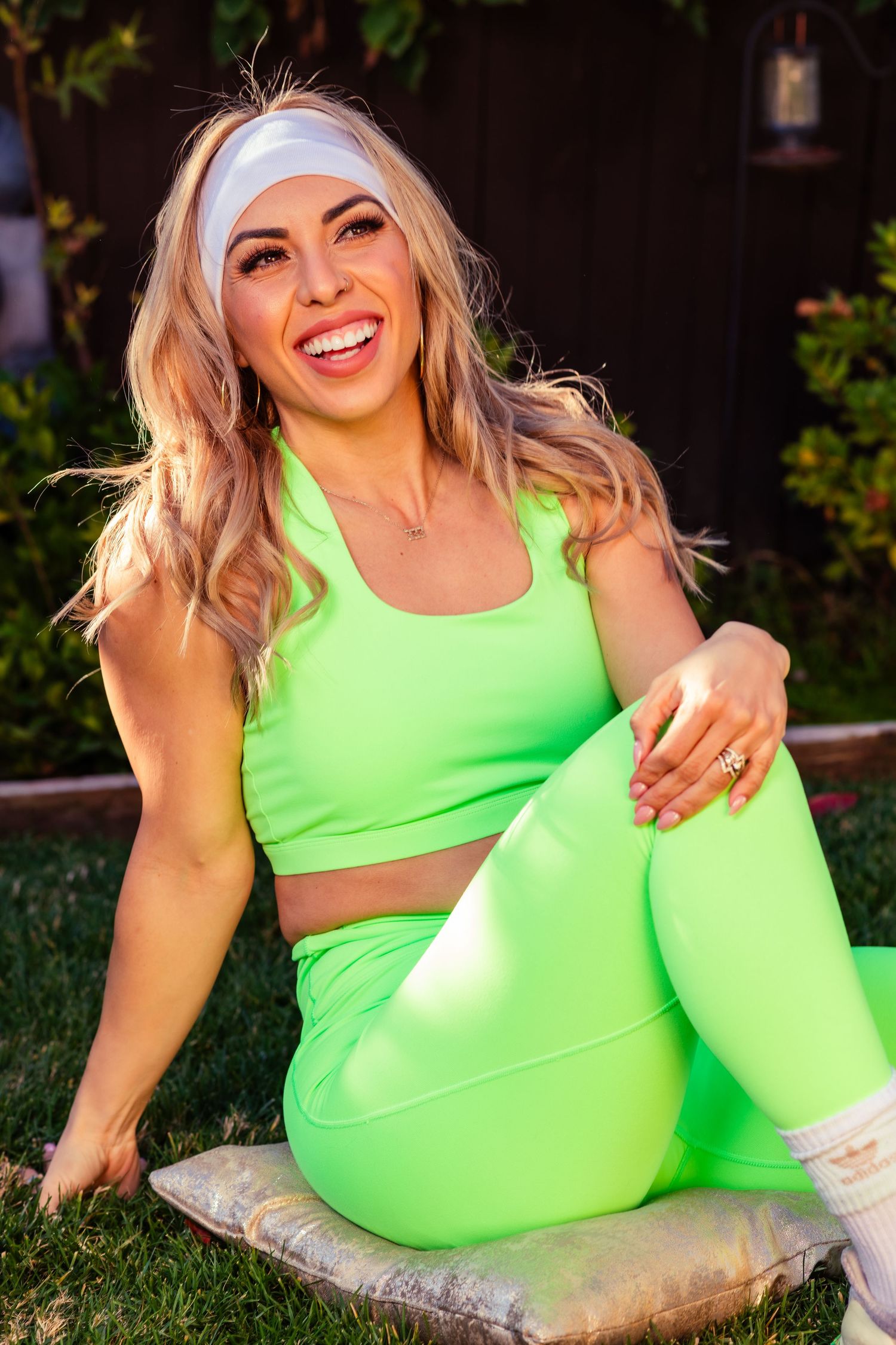 Athletic woman in lime green workout set smiles while lounging on outdoor cushion.