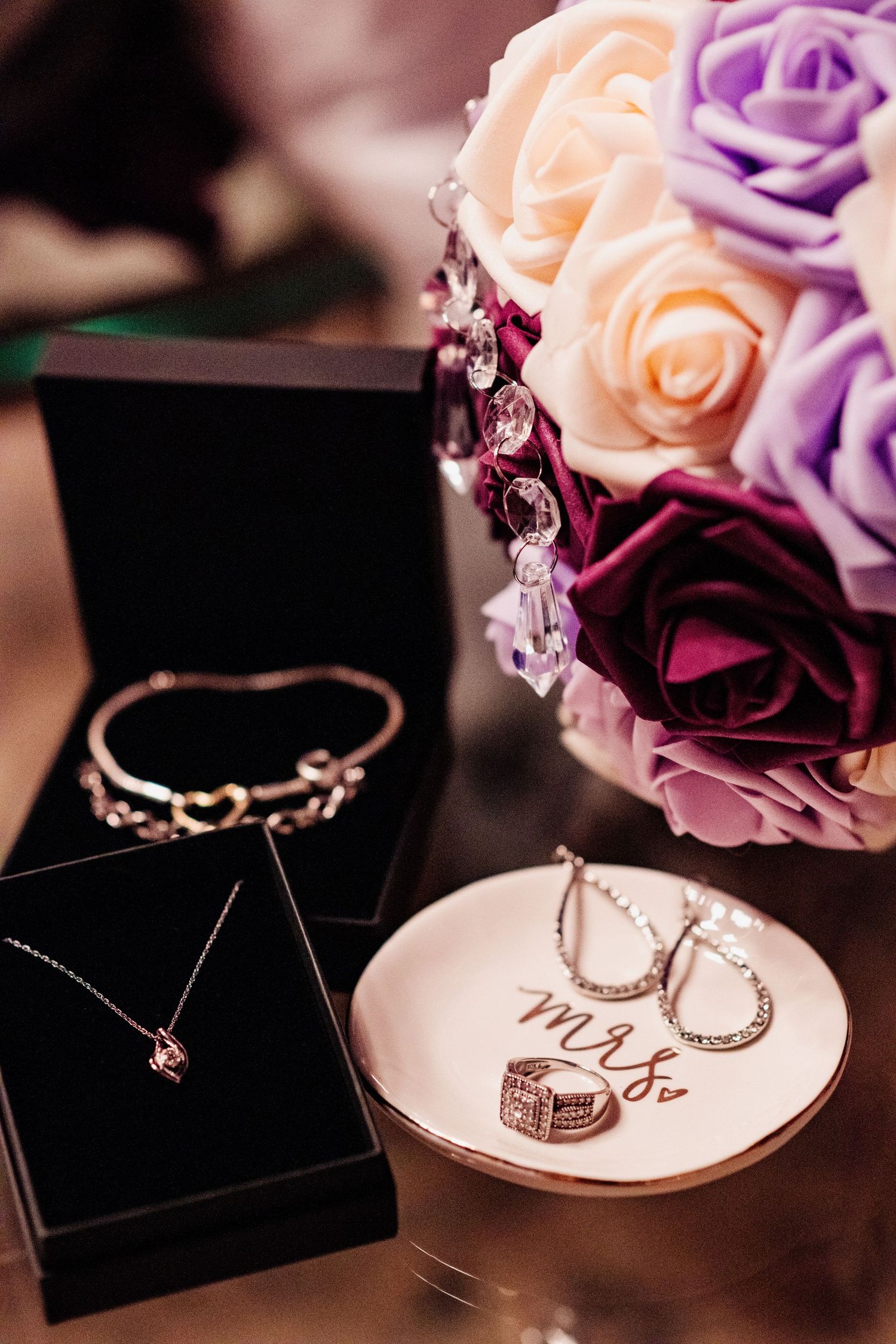 Wedding jewelry and accessories arranged with purple and pink roses.
