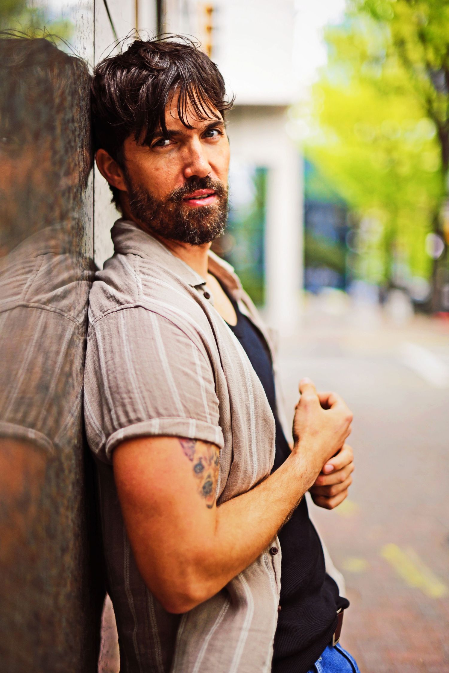 Person in sleeveless shirt leaning against wall outdoors in urban setting with natural lighting.