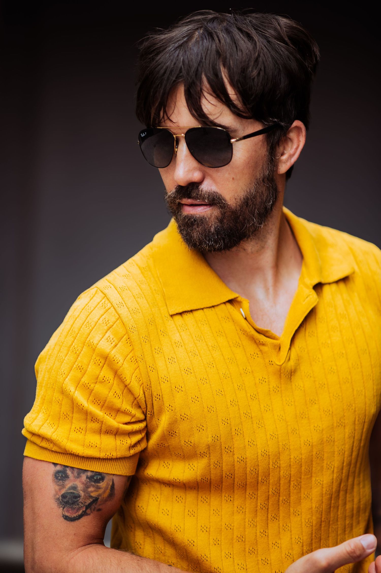 A close-up fashion shot shows a yellow knit polo shirt against a dark background.