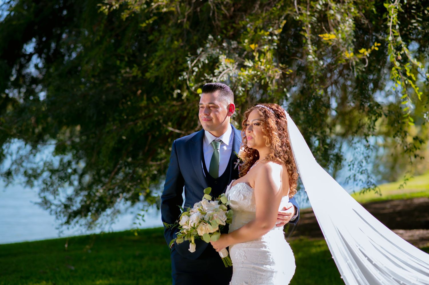 Tender wedding moment captured in a sun-drenched garden setting with flowing white veil.