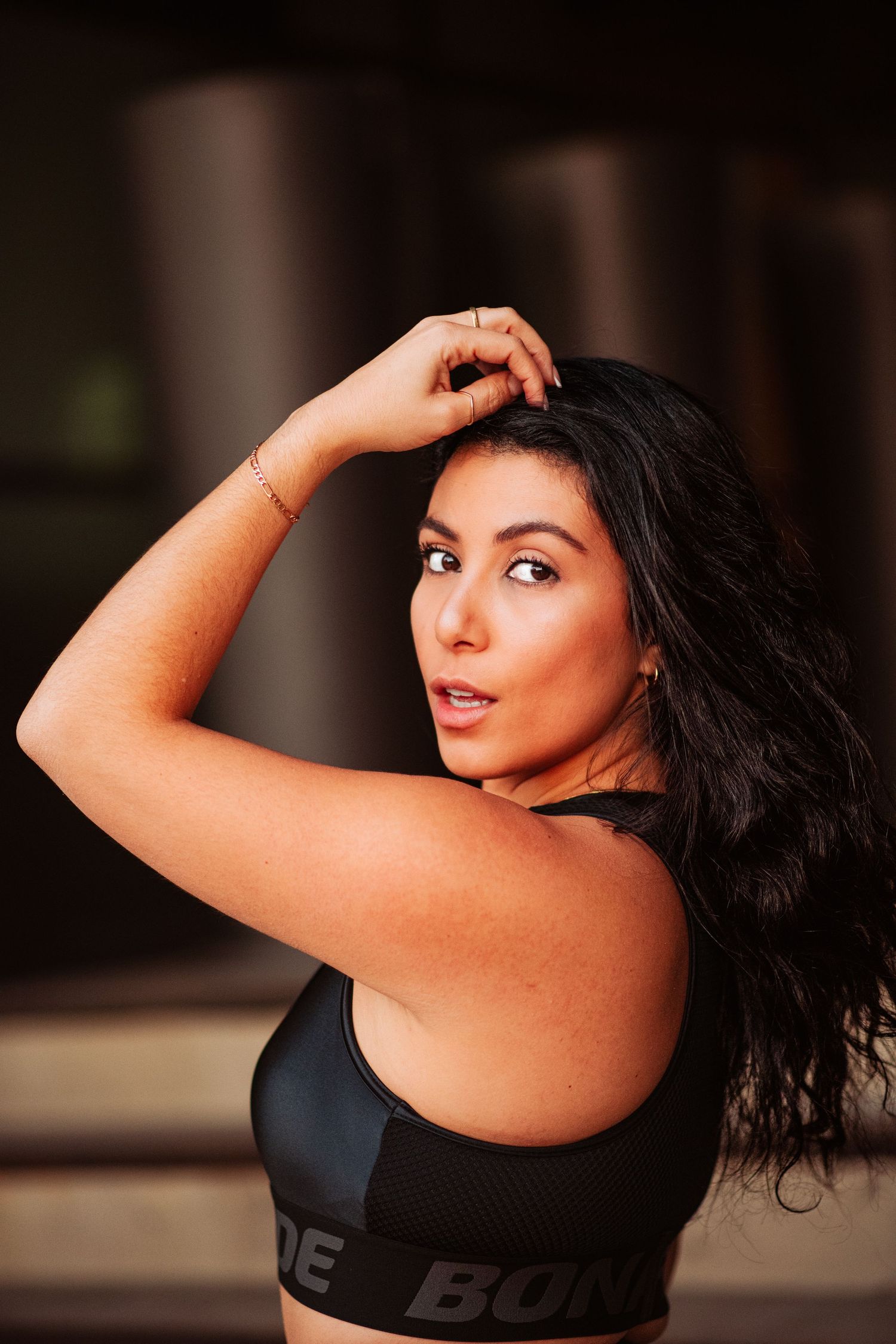 Alessandra Taryn
Athletic woman in black sports bra  Bona Fide the brand posing and showing off her arm muscles against blurred background.