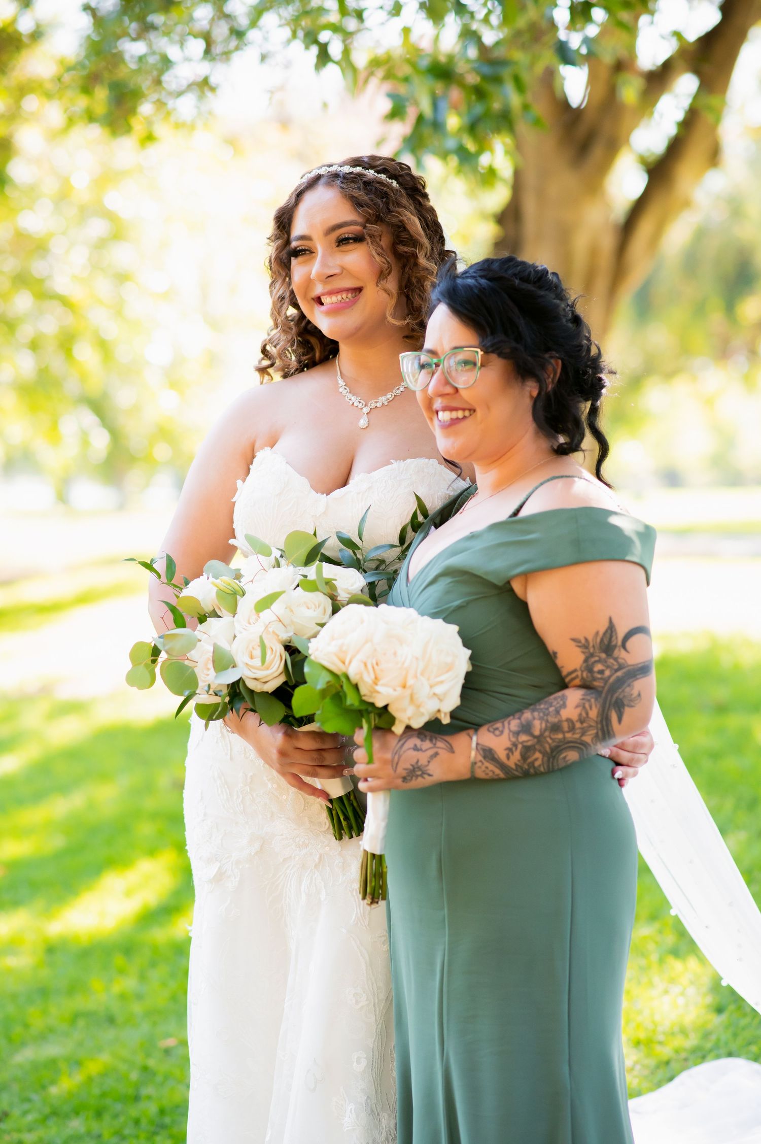 Wedding party members in sage green dresses and white gown pose with bouquets during outdoor photo session.