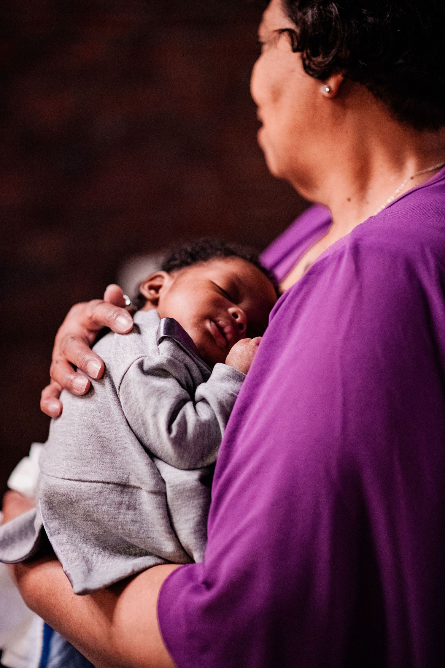 A series of photos shows a sleeping newborn baby in gray swaddling being held against a person wearing purple clothing.