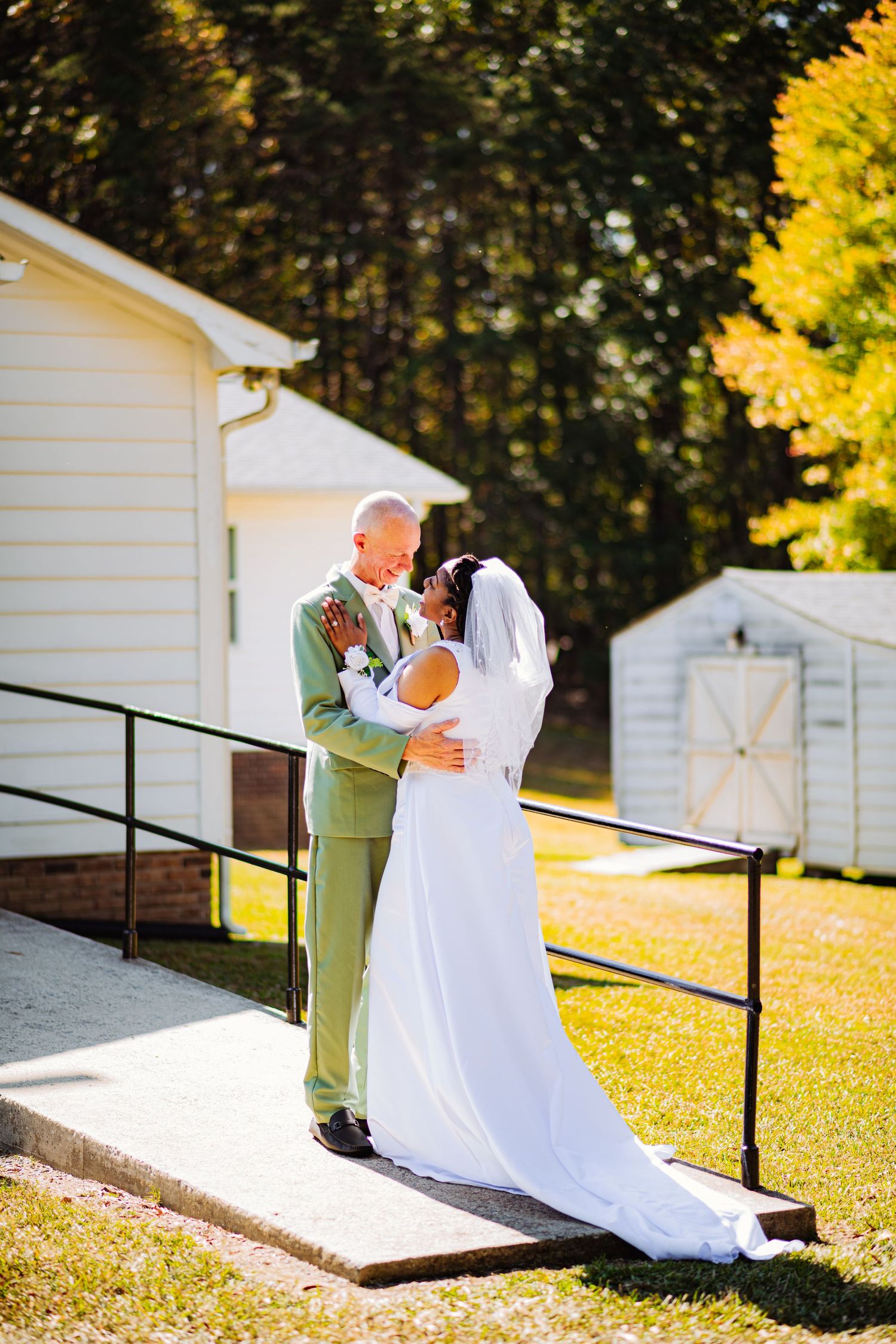 A romantic outdoor wedding moment between newlyweds on a ramp outside a white building on a sunny autumn day.