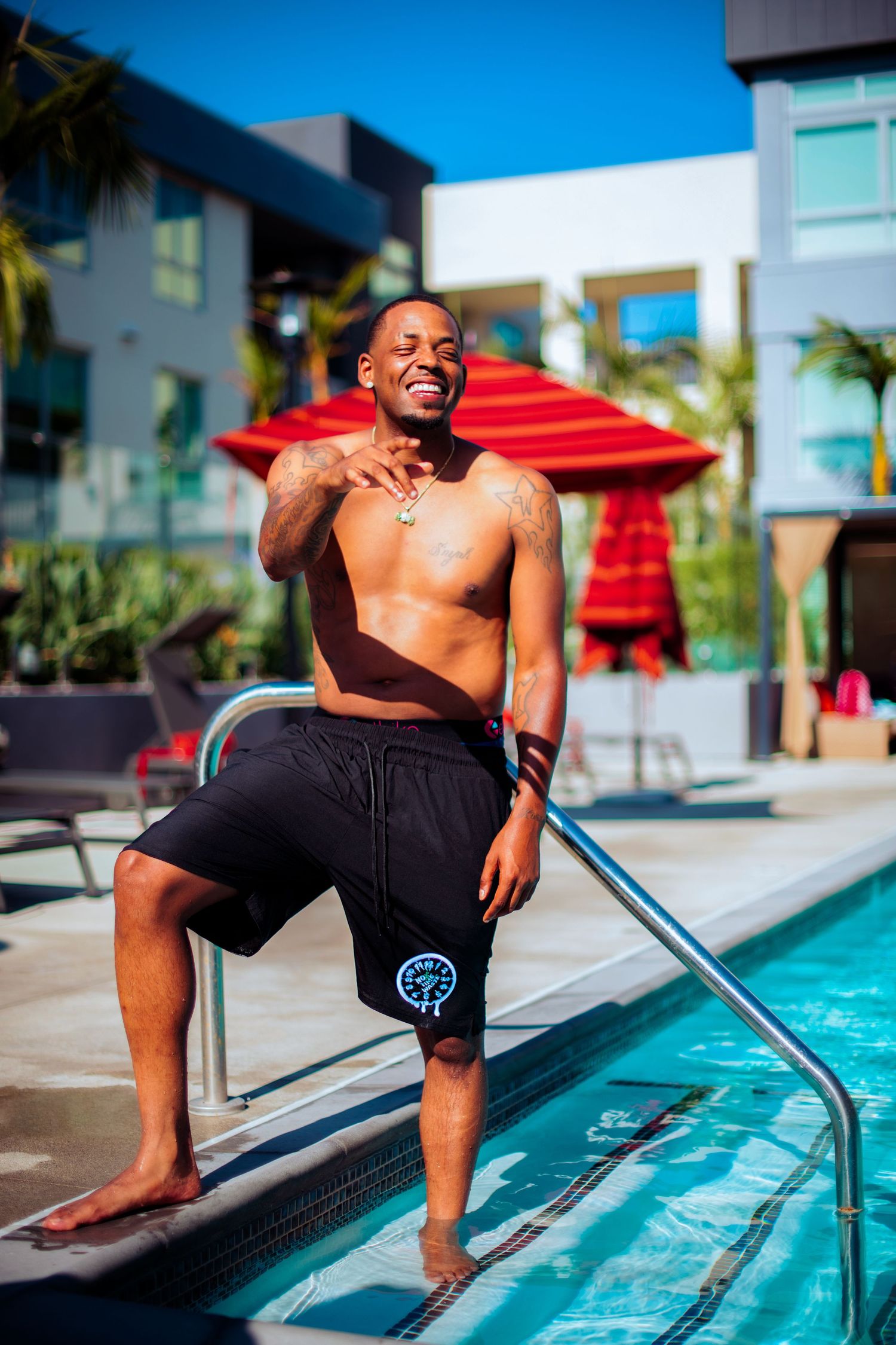Person in black shorts relaxing by modern pool with palm trees in background.