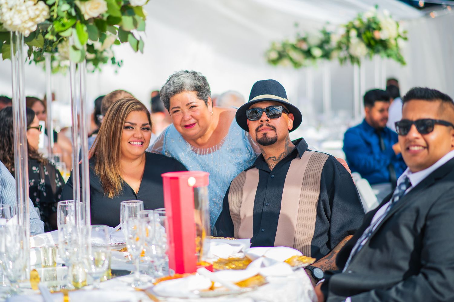 Wedding reception under white tent with elegant table settings and floral centerpieces.