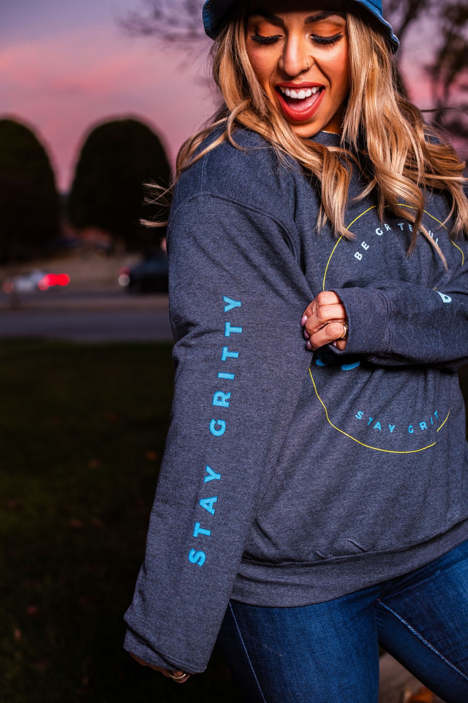 Close-up of gray sweatshirt with Stay Gritty text and blue bucket hat at dusk.