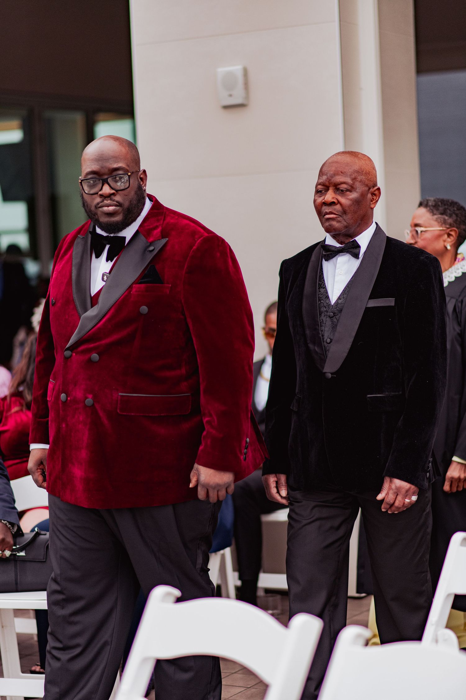 A group wearing formal attire with red velvet jackets and black suits stands together at an event.