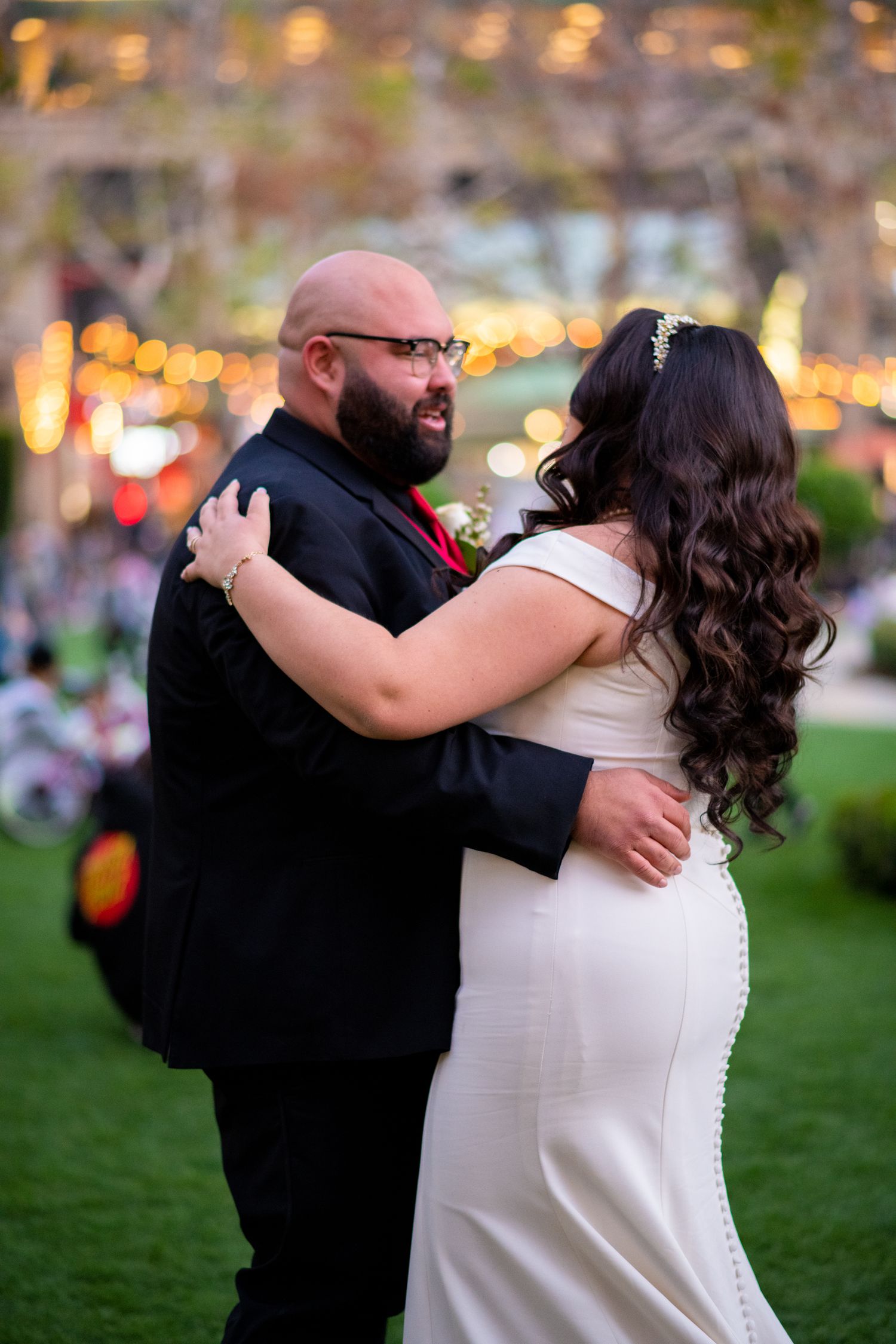 Couple embracing outdoors at dusk with twinkling lights in the background creating a romantic atmosphere.