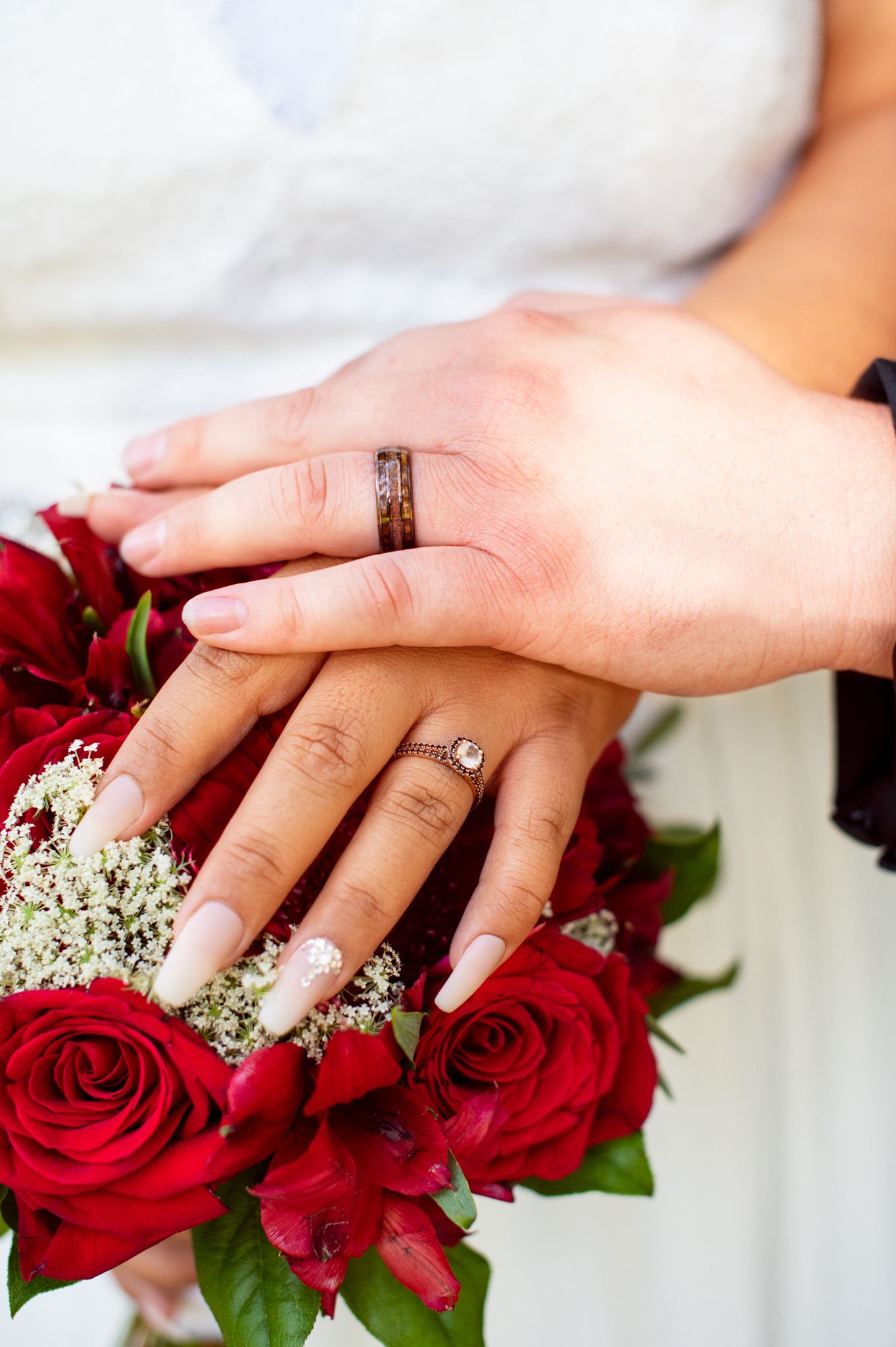 Close-up of hands with wedding rings resting on red rose bouquet.