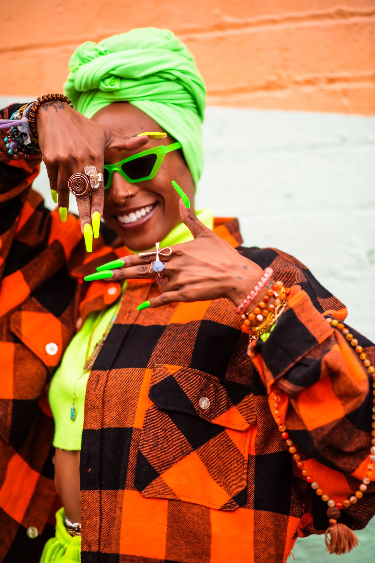 A K A $ H A A
woman wearing orange plaid shirt and neon headwrap smiles while posing against white background.