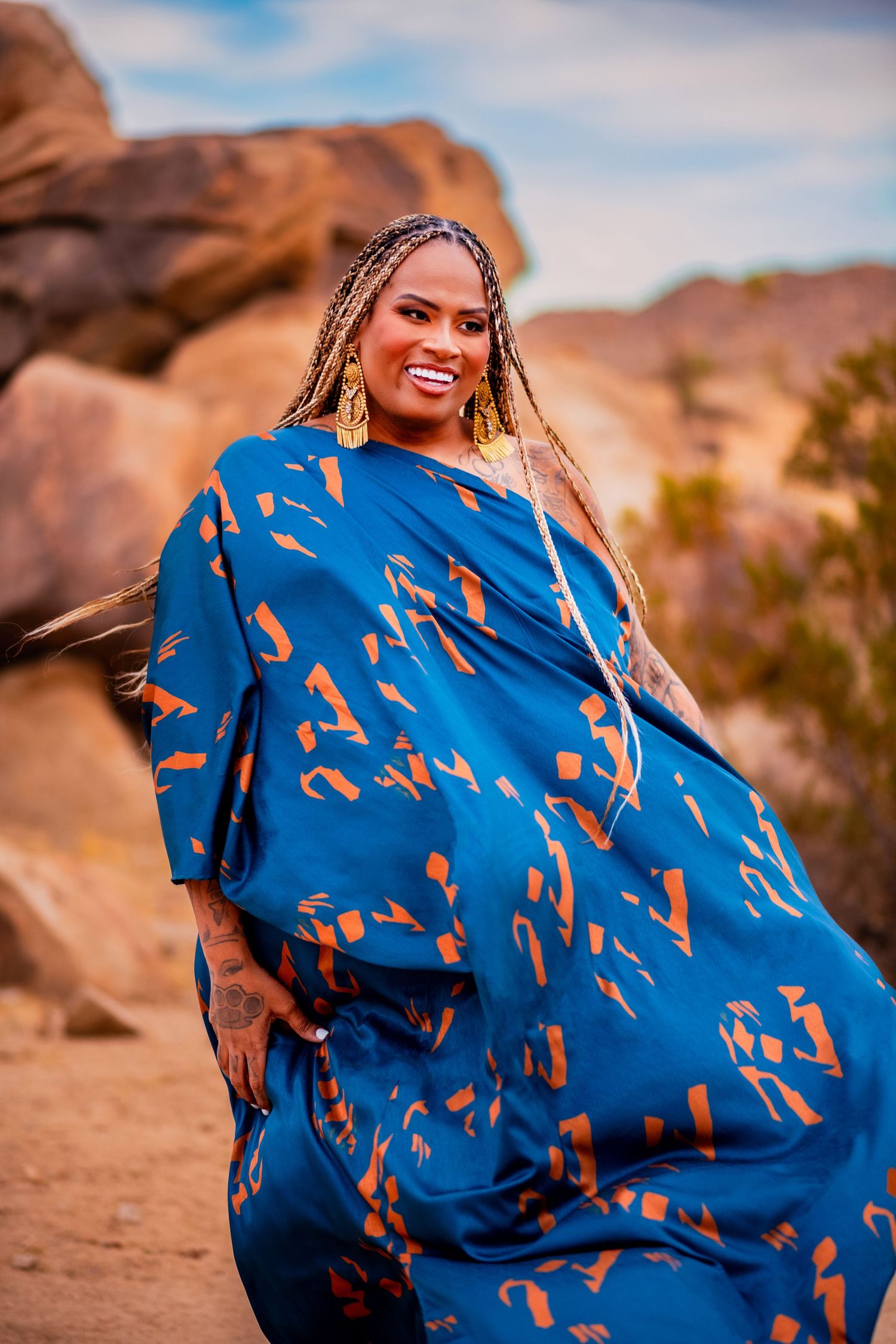 Fashion portrait in desert showing joyful pose in flowing blue patterned dress.