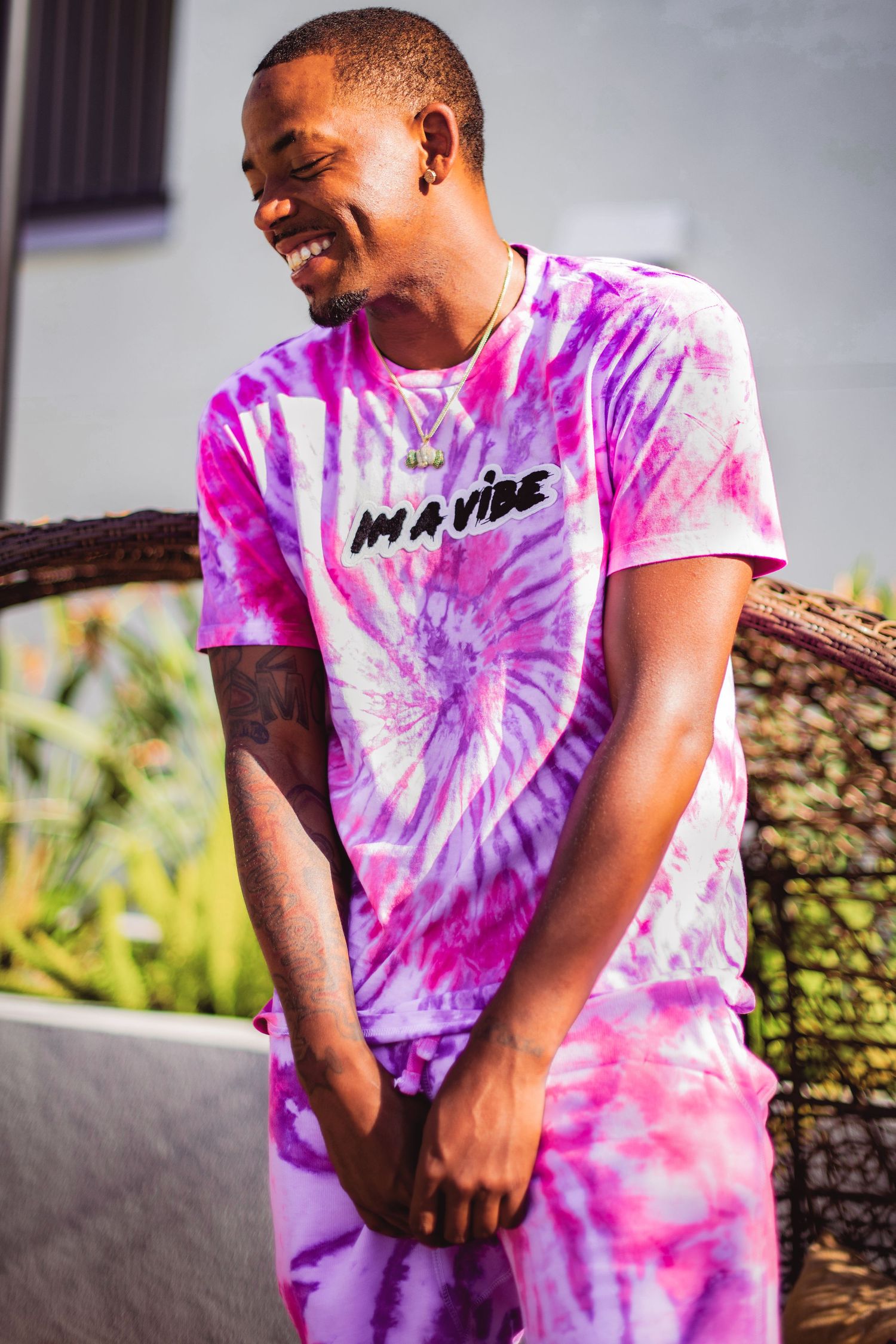 Person wearing a pink and purple tie-dye t-shirt sits outdoors in a casual pose.