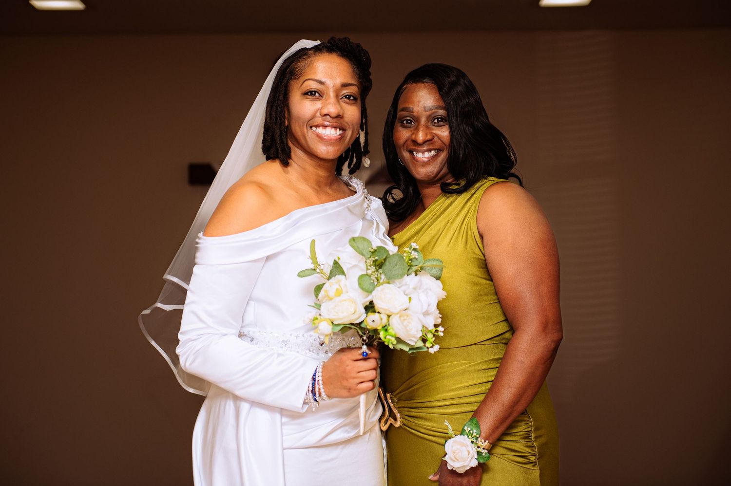 Wedding party members embrace and smile while wearing elegant white and chartreuse formal attire.