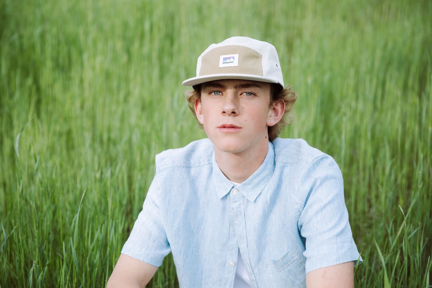 Person in casual attire sitting among tall green grass on sunny day.