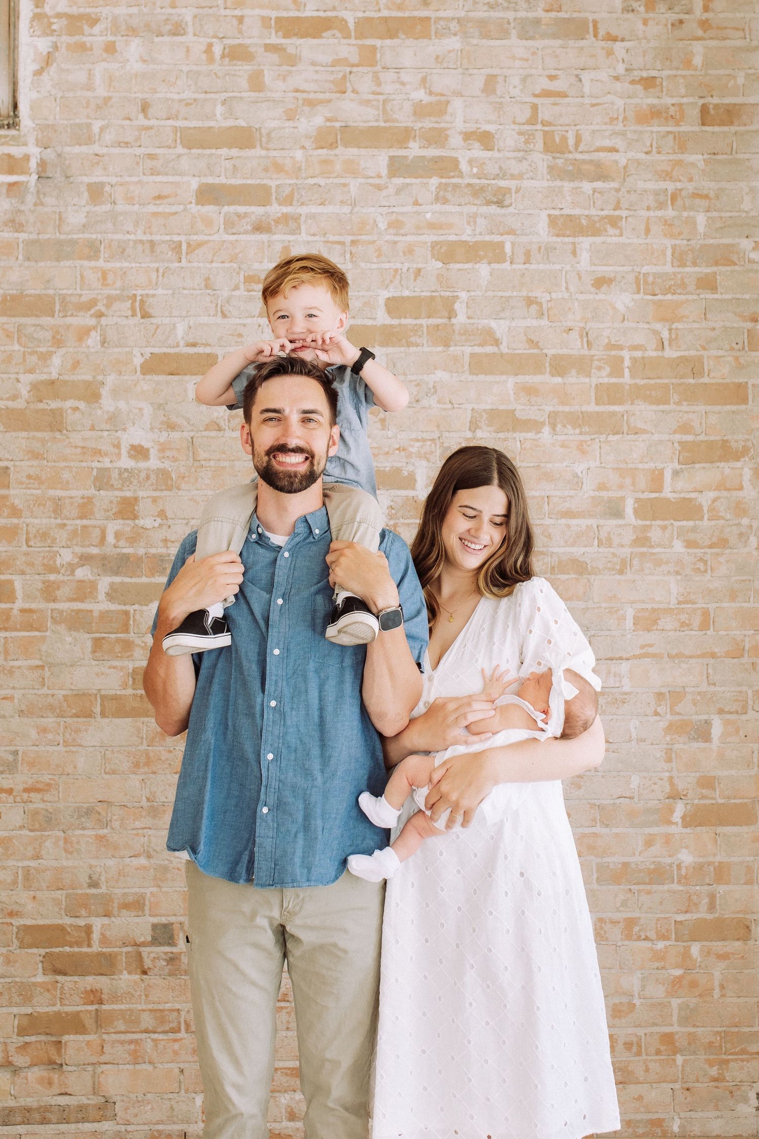 Family poses playfully against brick wall in studio setting.