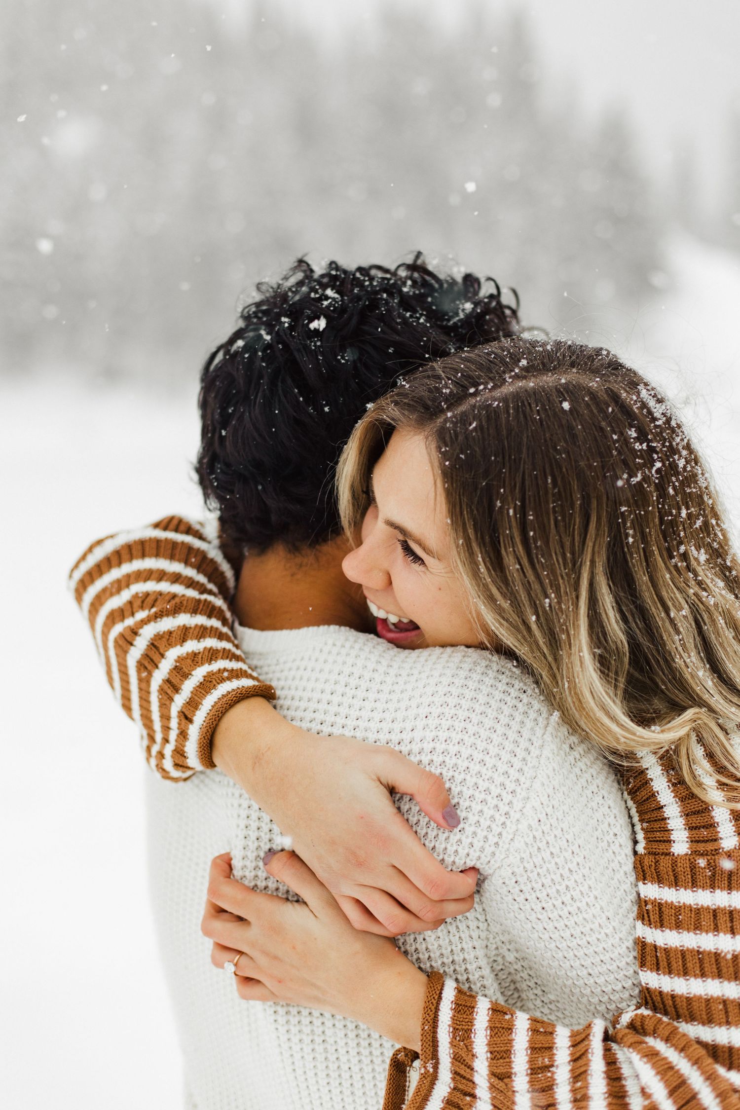 Two people embrace warmly while snow falls around them in winter.