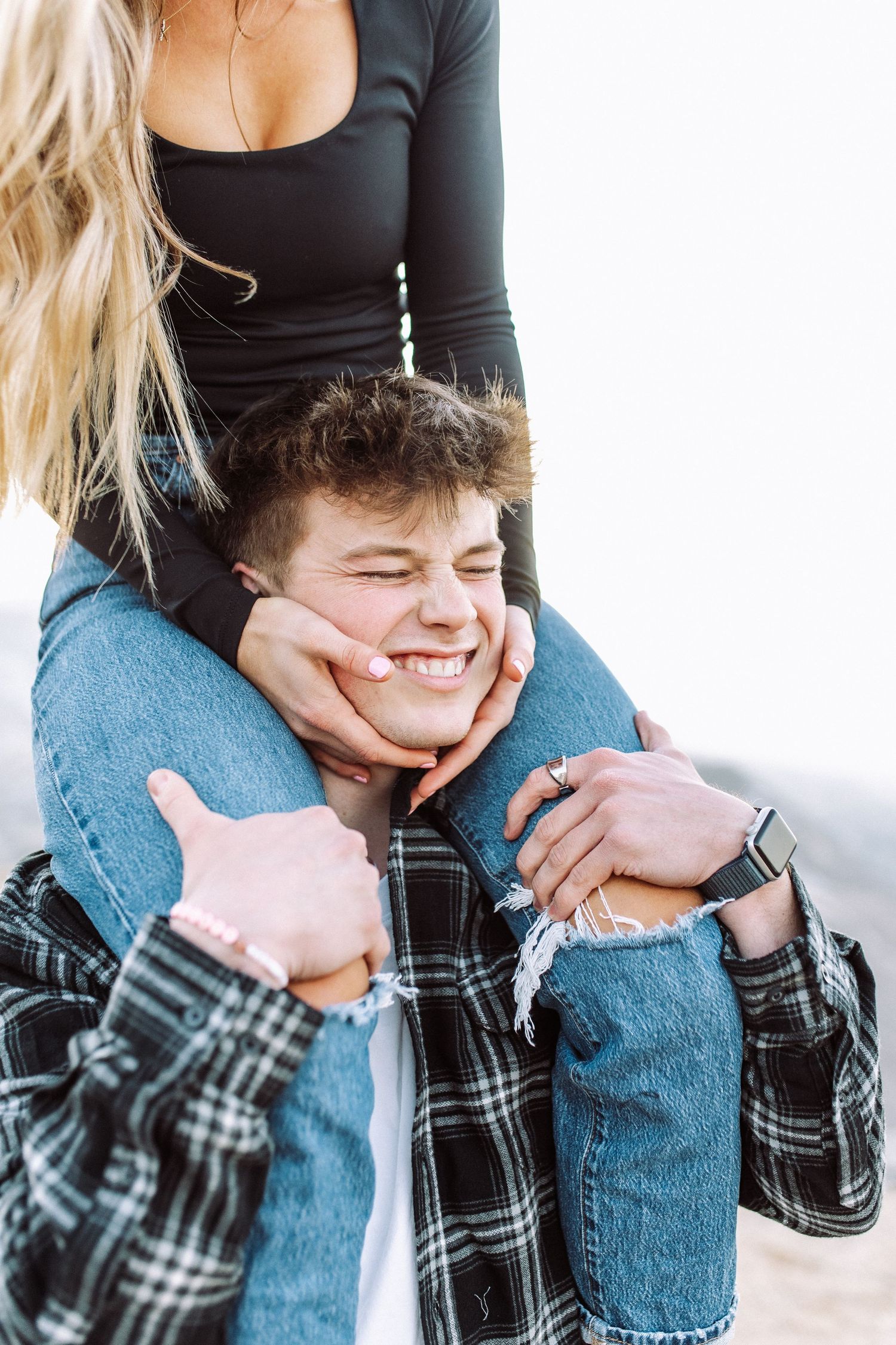 A playful couple shares a tender moment with hands cupping cheeks while wearing casual denim and plaid.