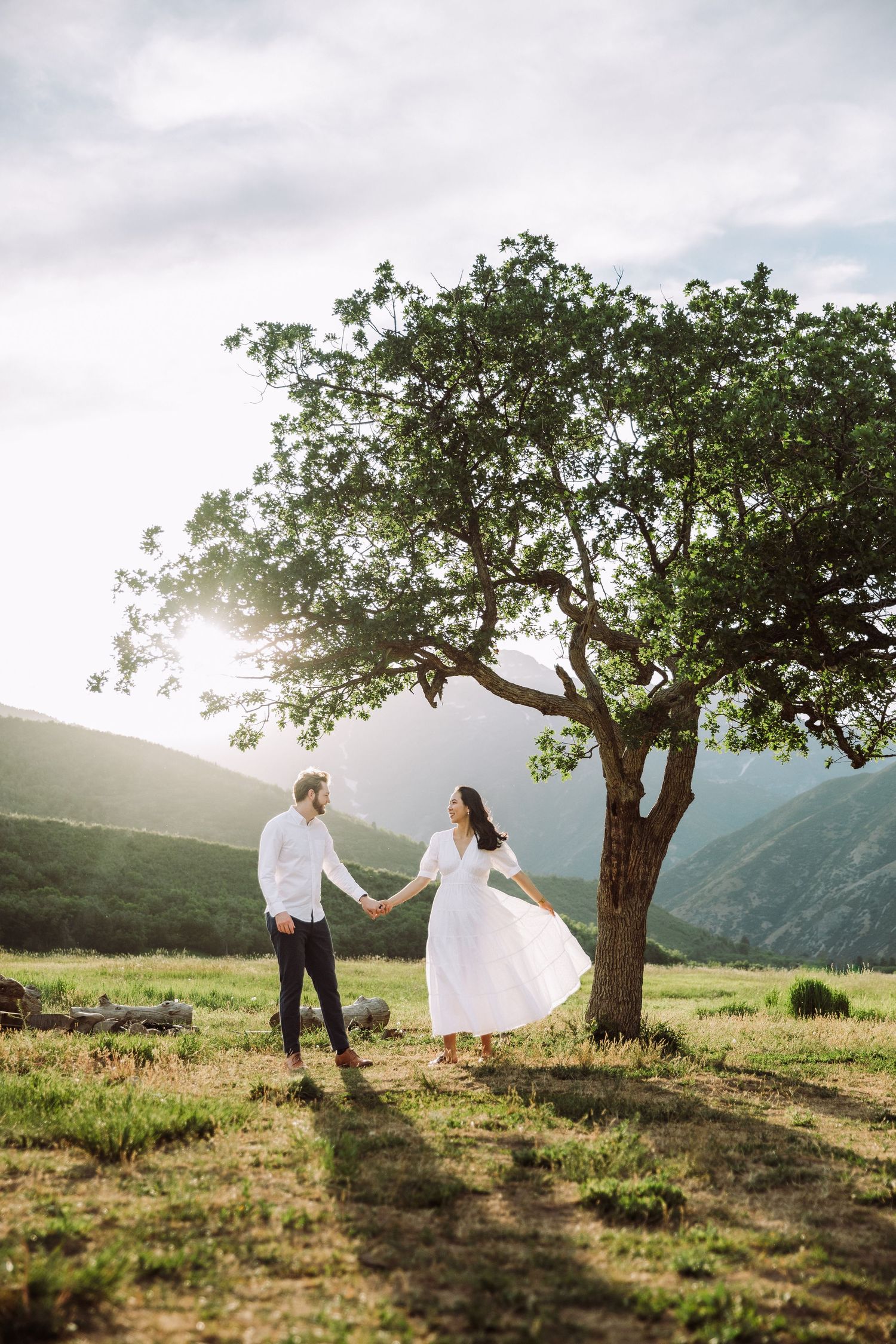 Couple dancing under large tree with mountain vista in background during golden hour.