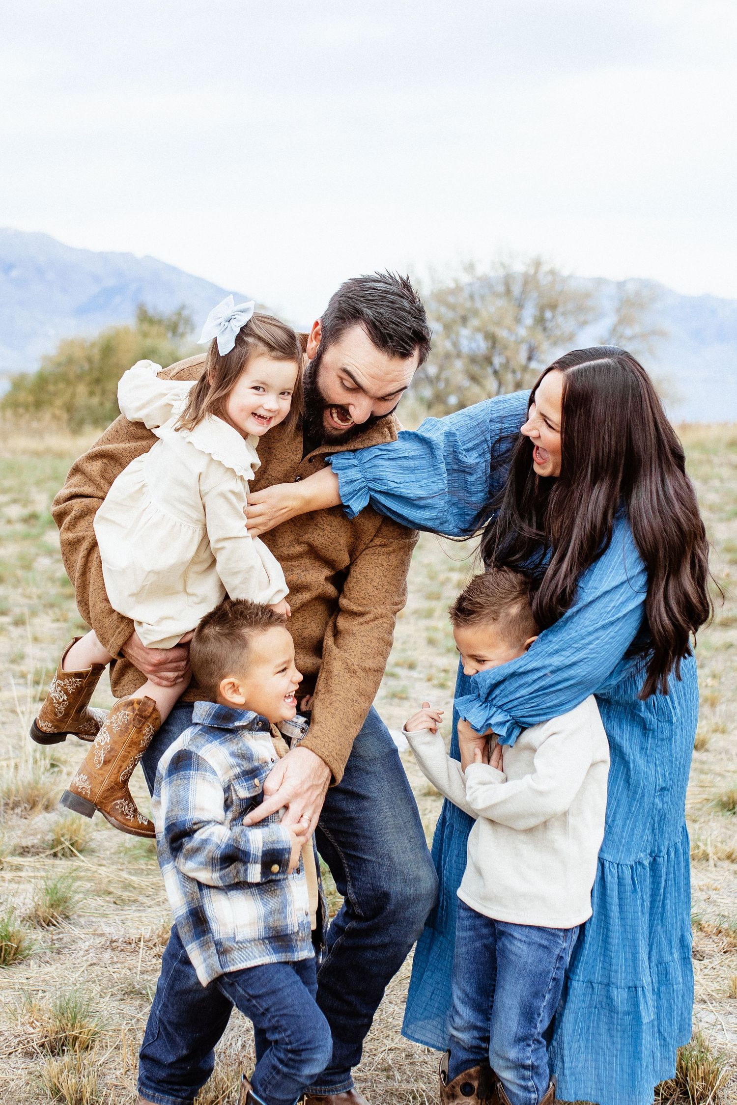 A playful family moment outdoors with mountains and blue sky in the background.