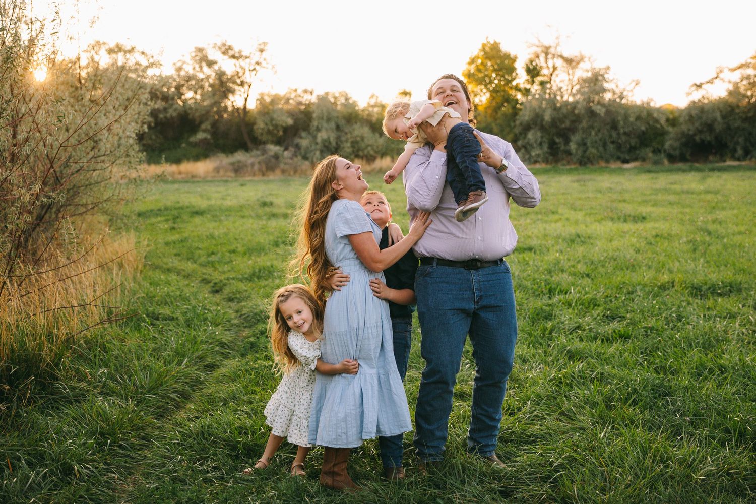 A couple and their dog share a tender moment in a sunlit meadow at golden hour.