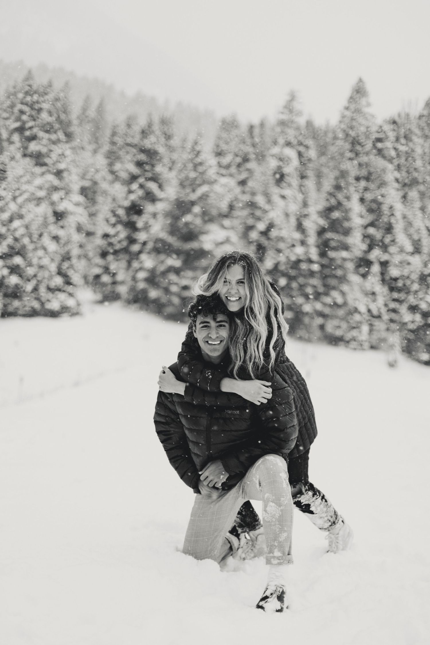 A playful couple enjoys themselves in deep snow during a winter photoshoot.