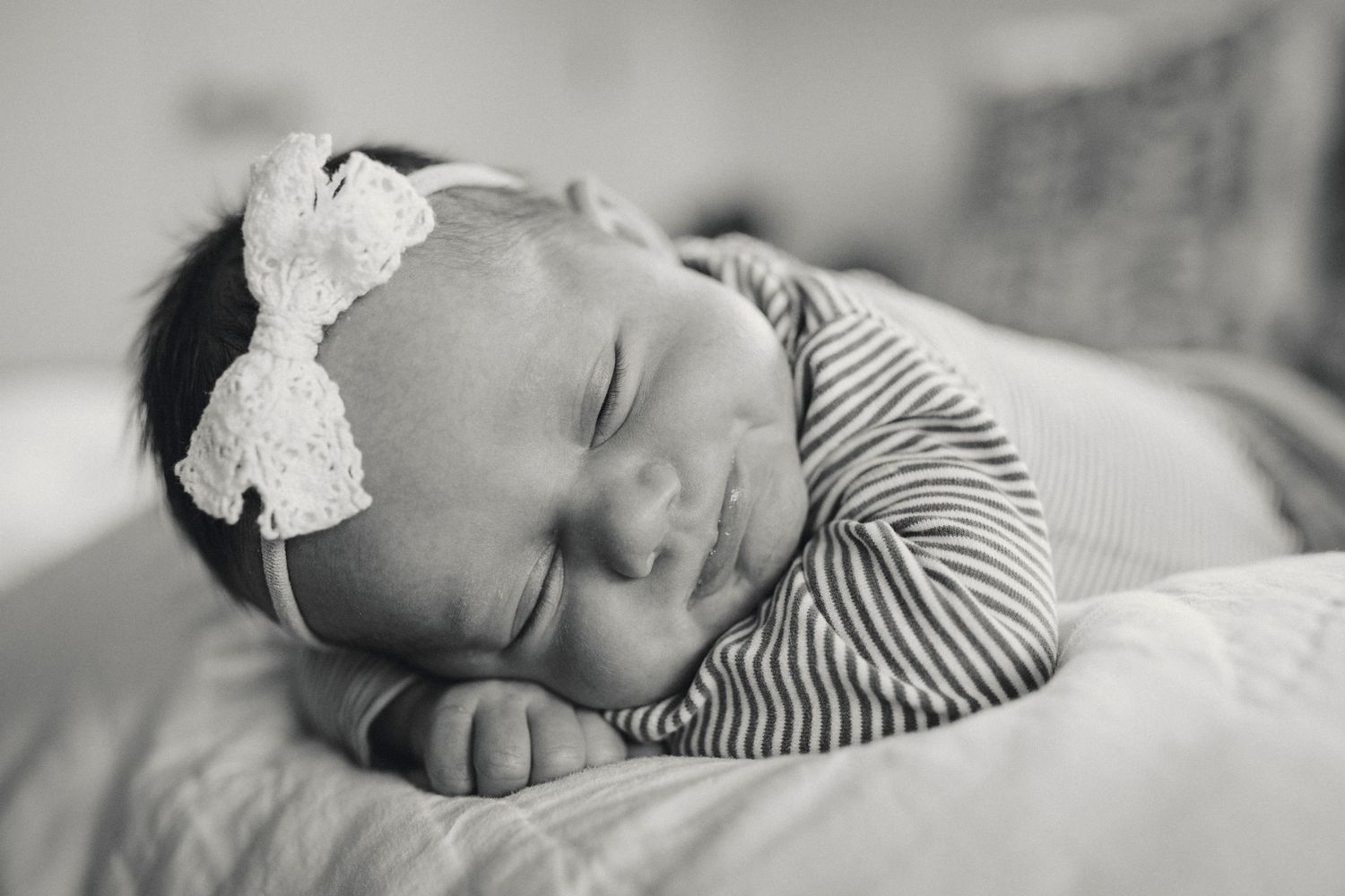 Peaceful sleeping baby wearing striped outfit and white bow headband.