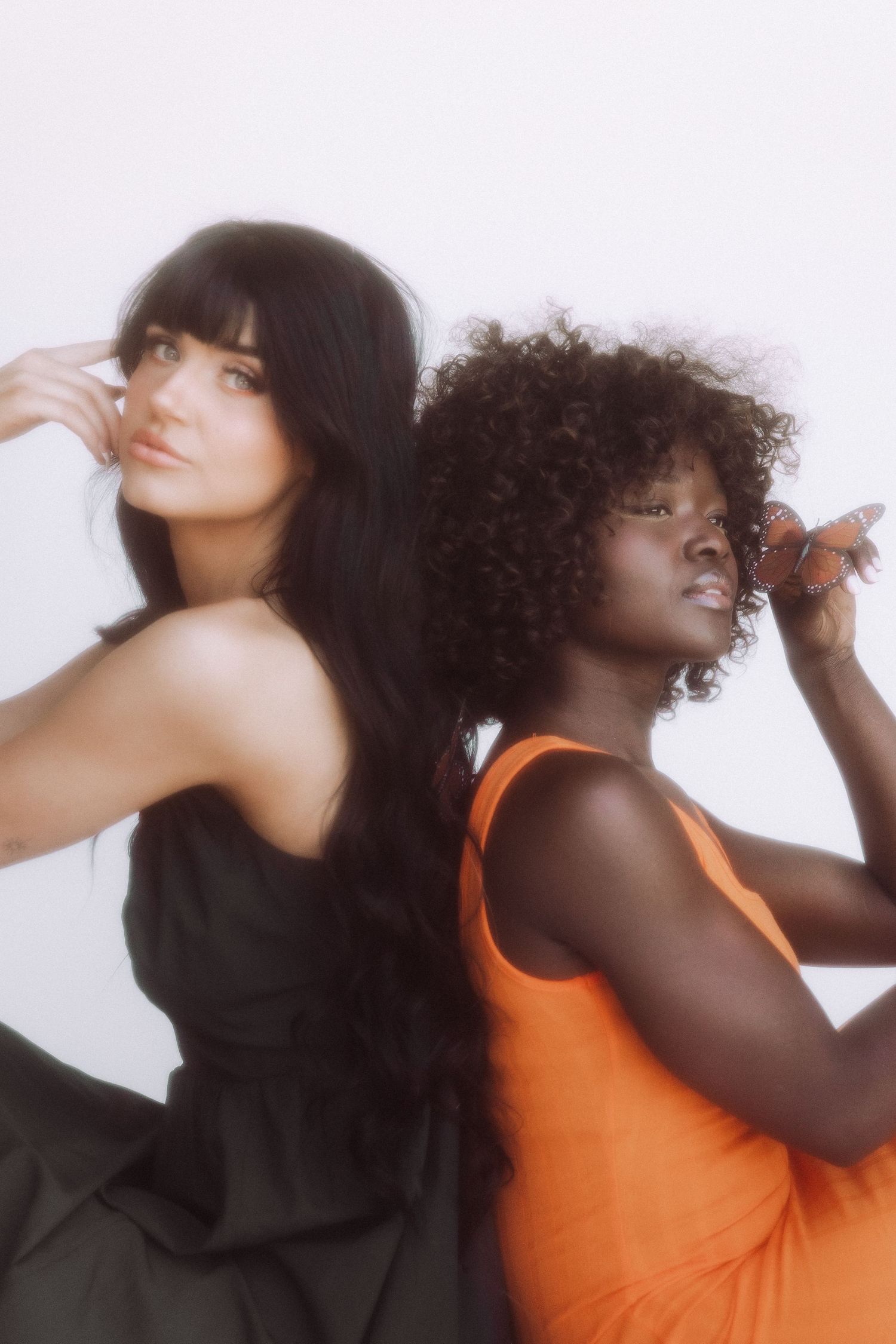 Two models in contrasting black and orange outfits pose artistically against white background.