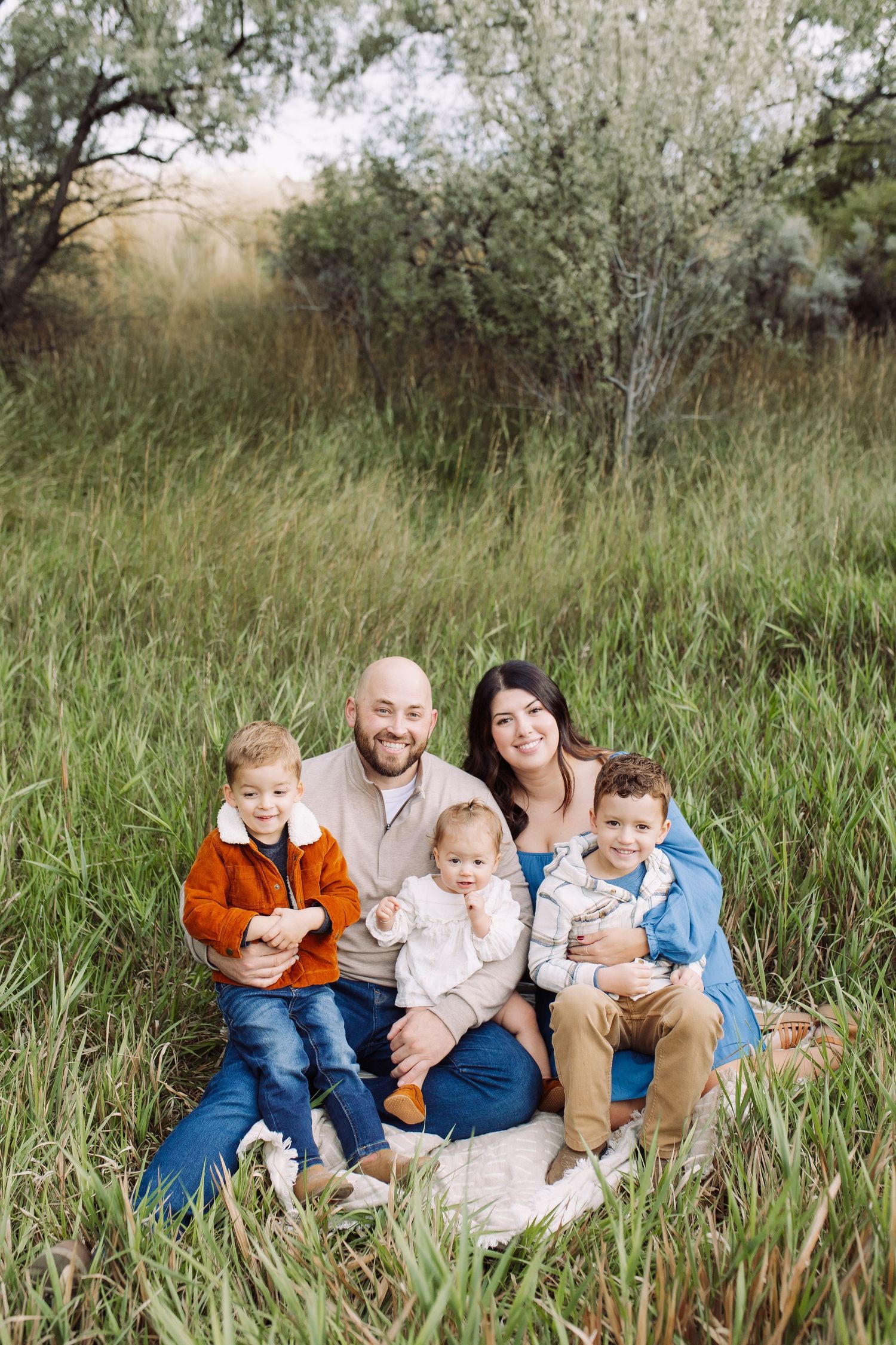 Family sitting together in tall grass during golden hour outdoor photo session.