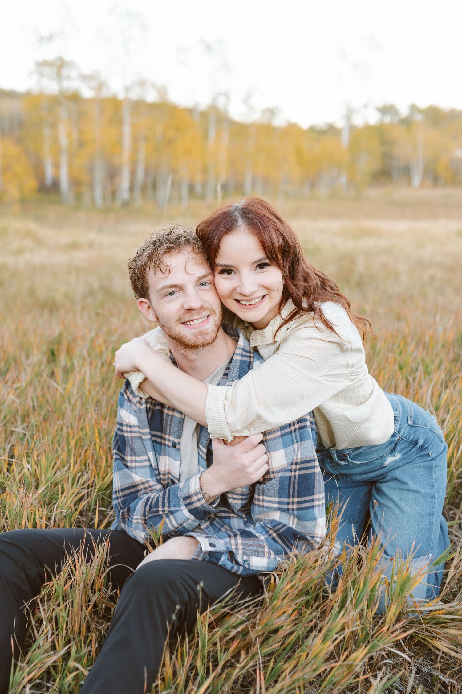 Couple shares joyful embraces in autumn grass with aspen trees behind.
