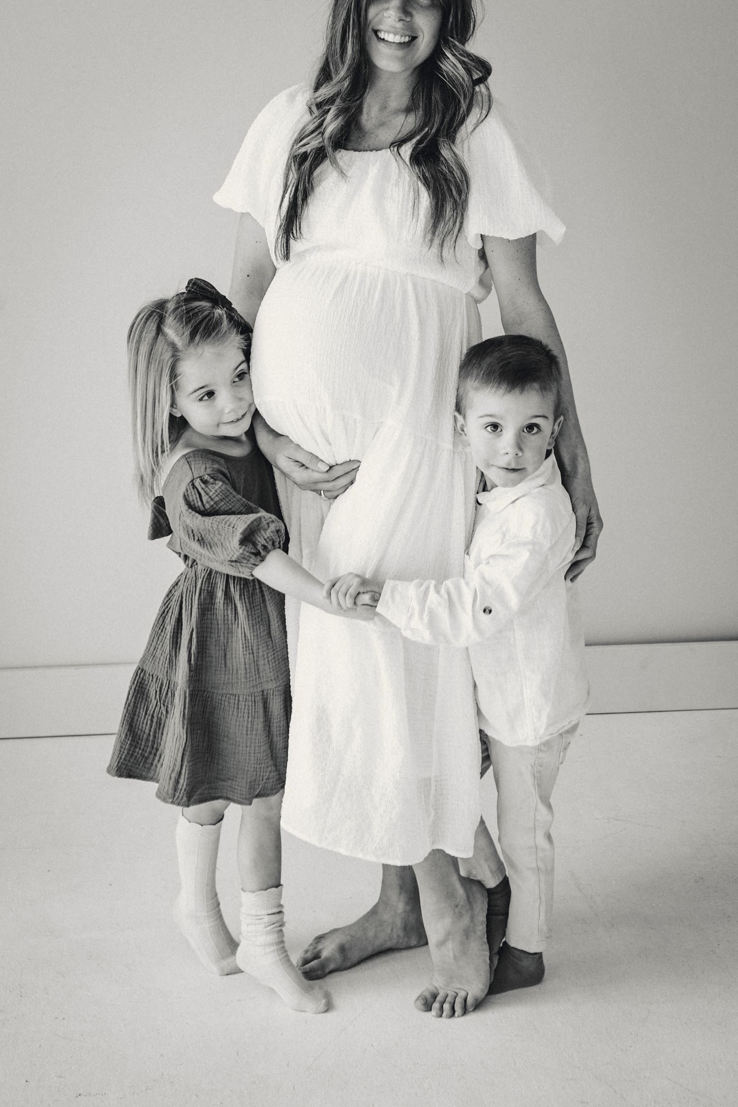 Black and white portrait of pregnant mother with two children in studio setting.