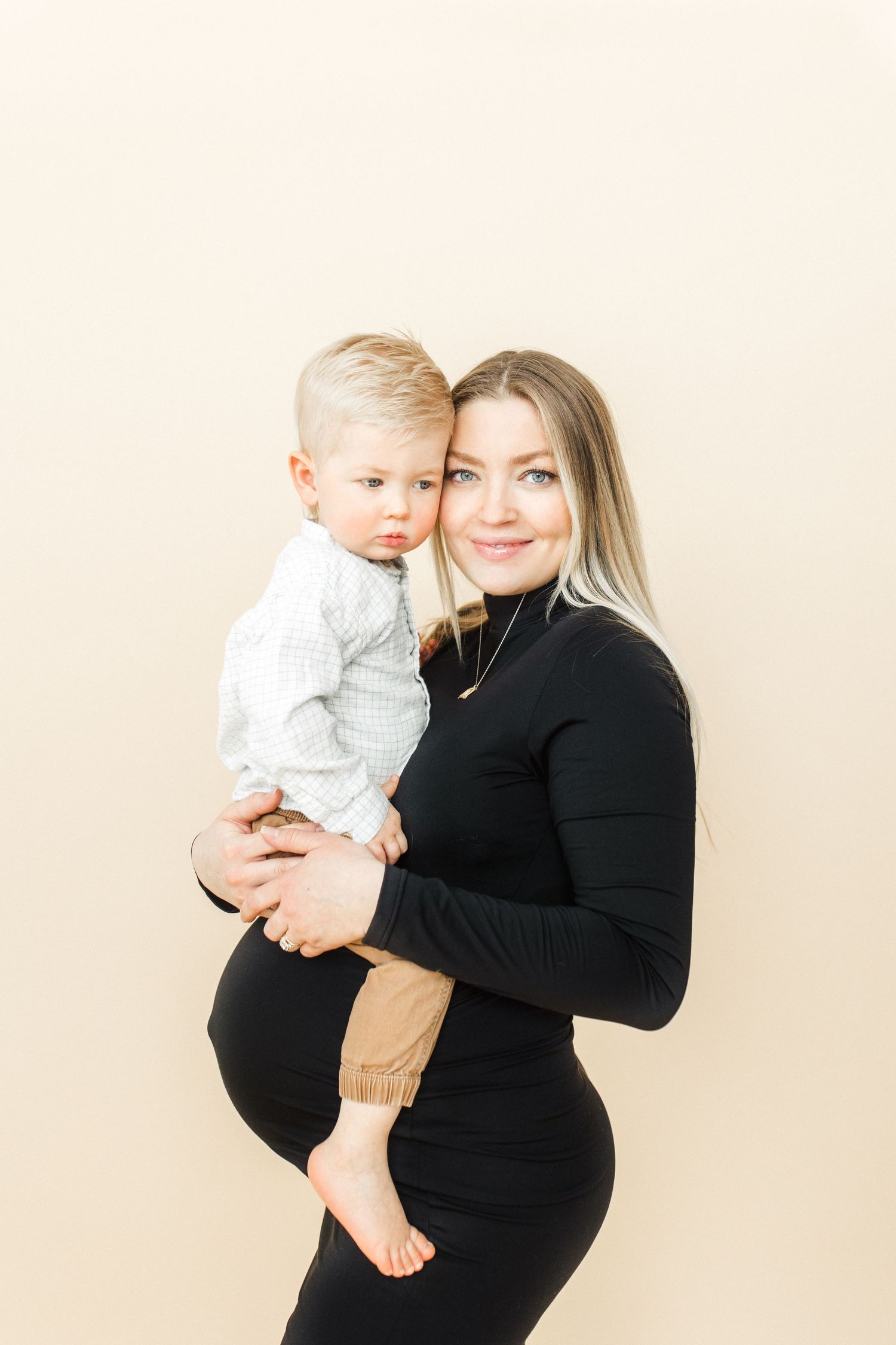 Studio maternity photos with toddler against cream background.